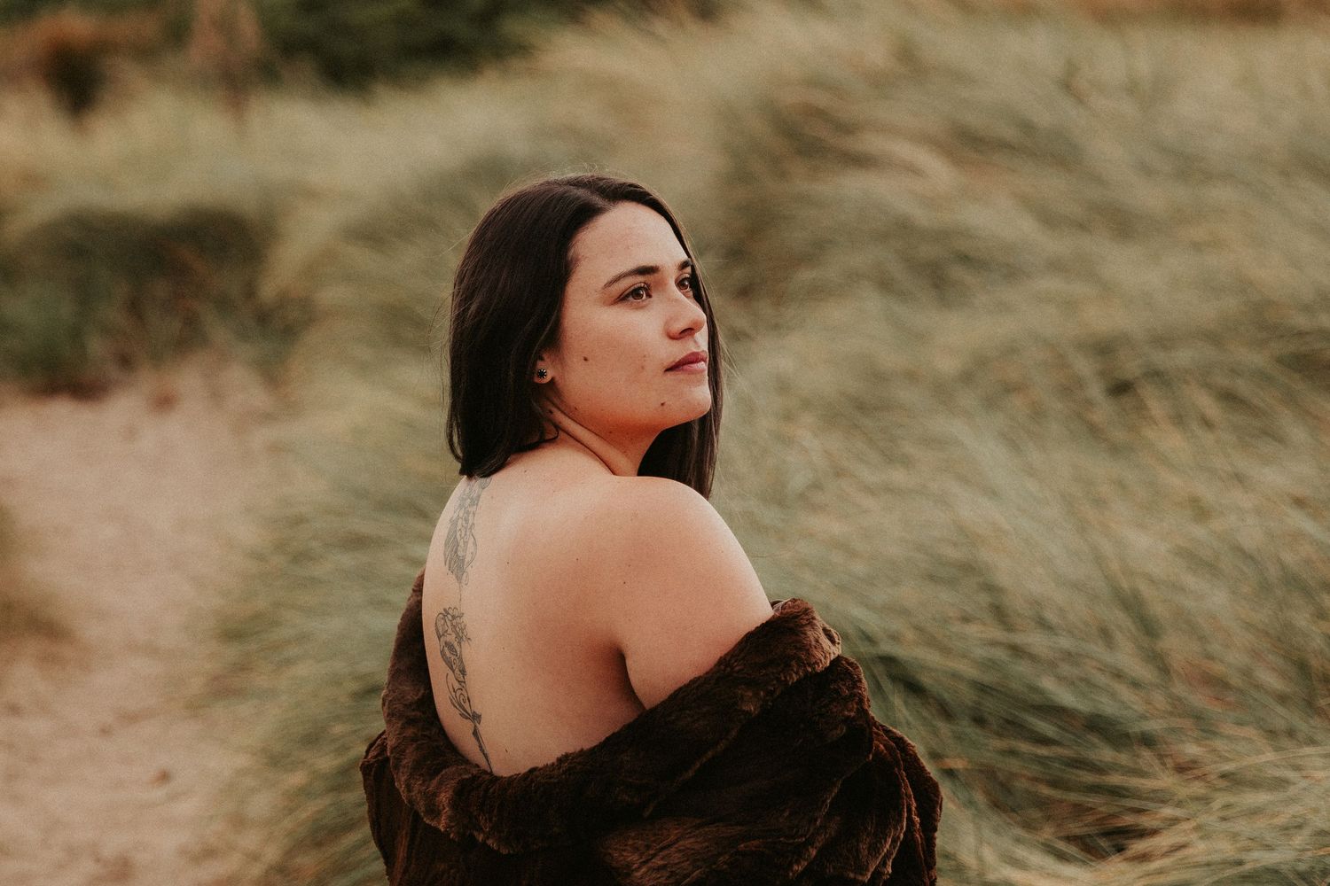 Artistic portrait session on coastal dunes with soft natural lighting and earth tones.