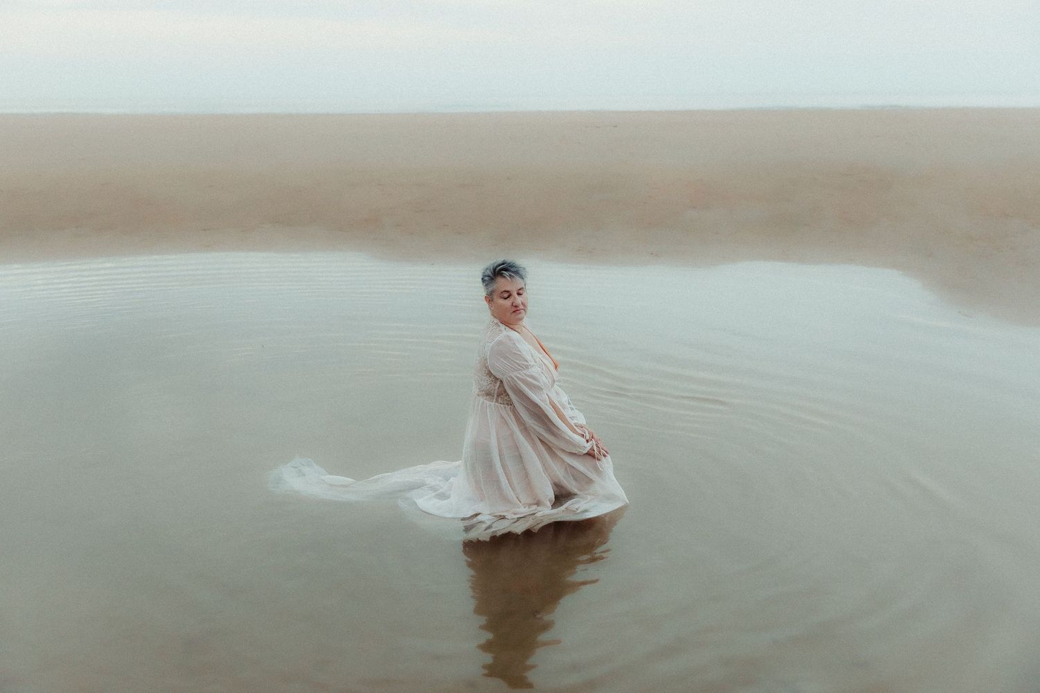 Figure in light dress spins gracefully in shallow water creating ripples.