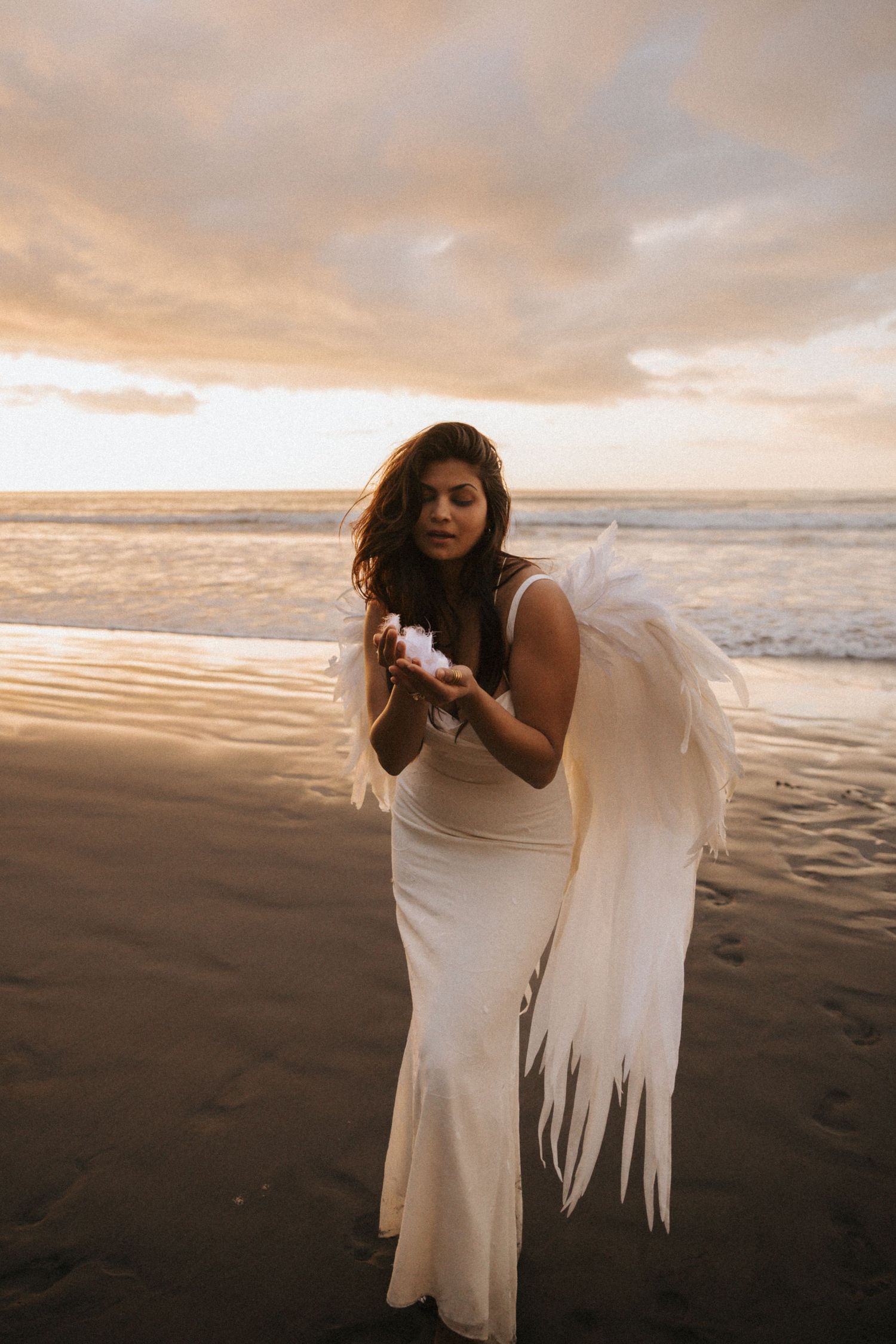 A figure in a flowing white dress poses gracefully against a moody sunset beach backdrop.
