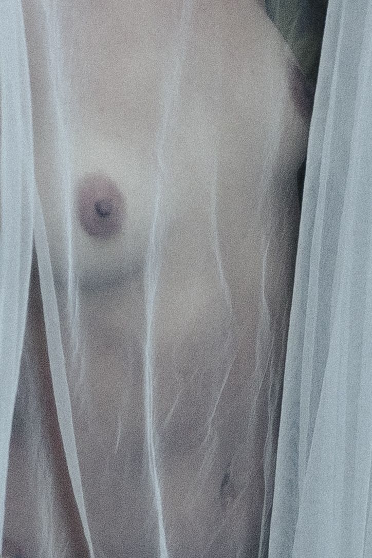Ethereal figure draped in sheer white fabric against dark background creating artistic contrast.