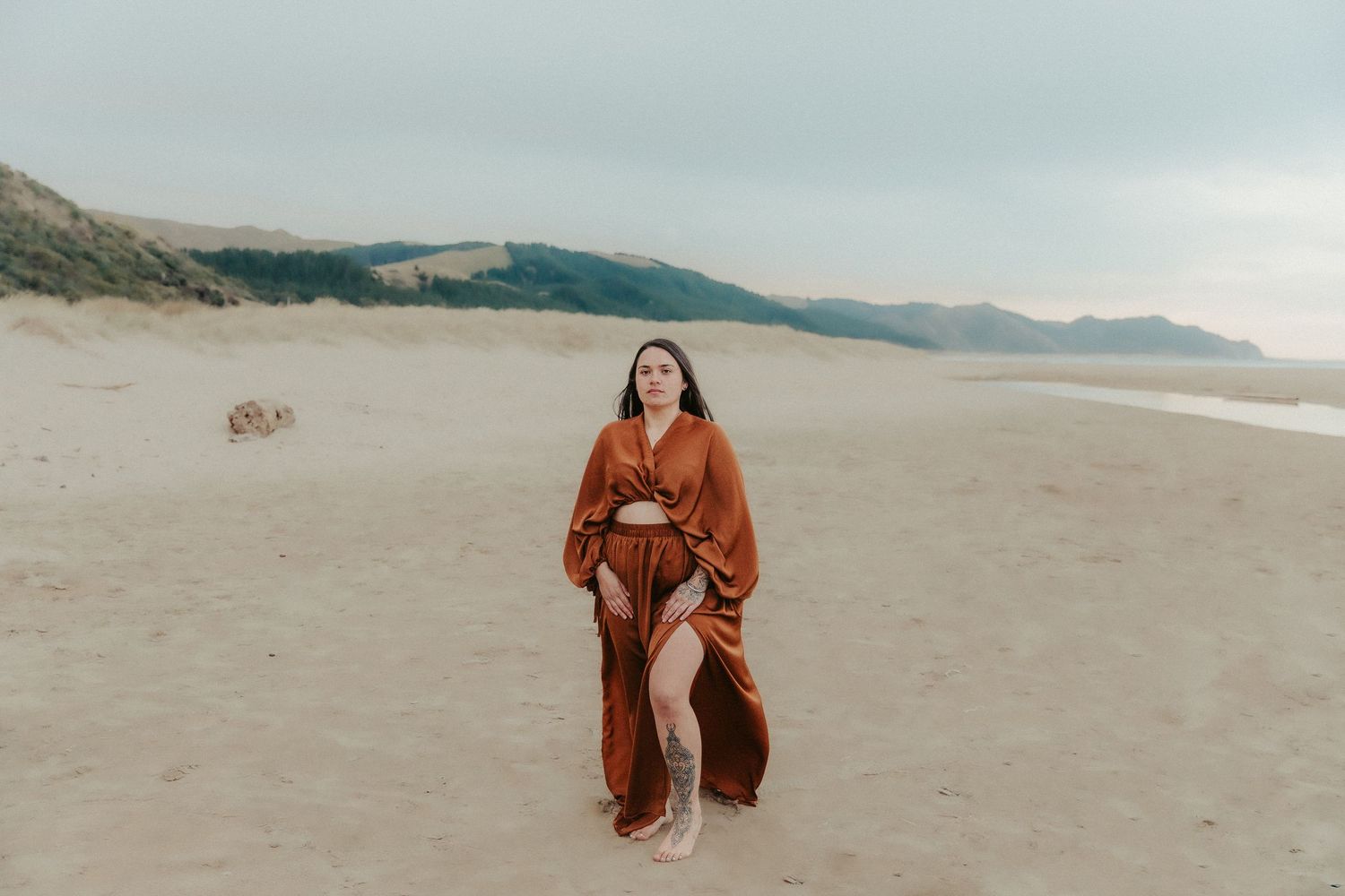 Artistic sequence of poses in terracotta dress against dramatic beach landscape.