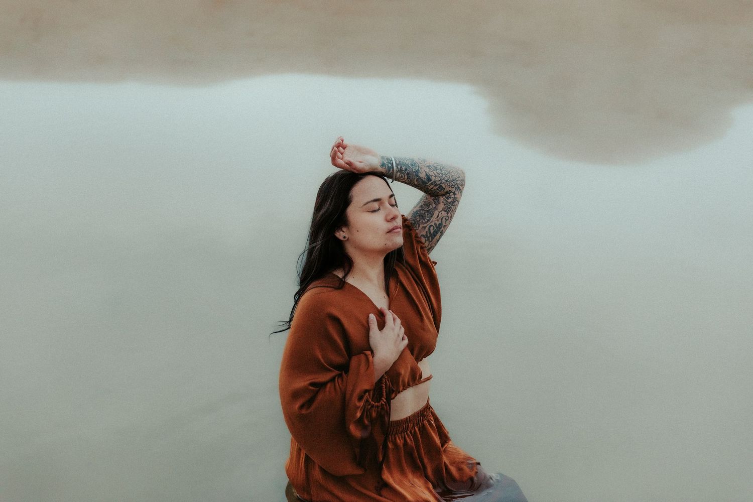 Figure in rust-colored outfit poses expressively against muted background.