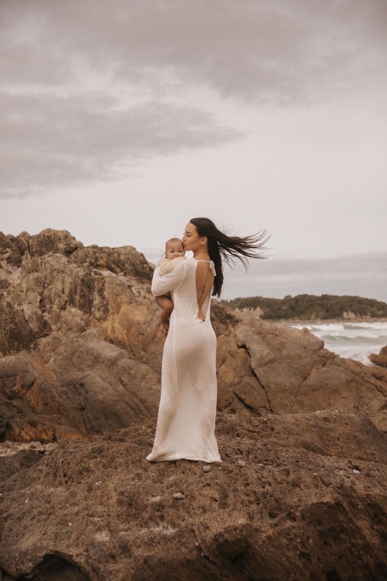 Flowing white dress catches the wind against dramatic rocky coastline and moody sky.