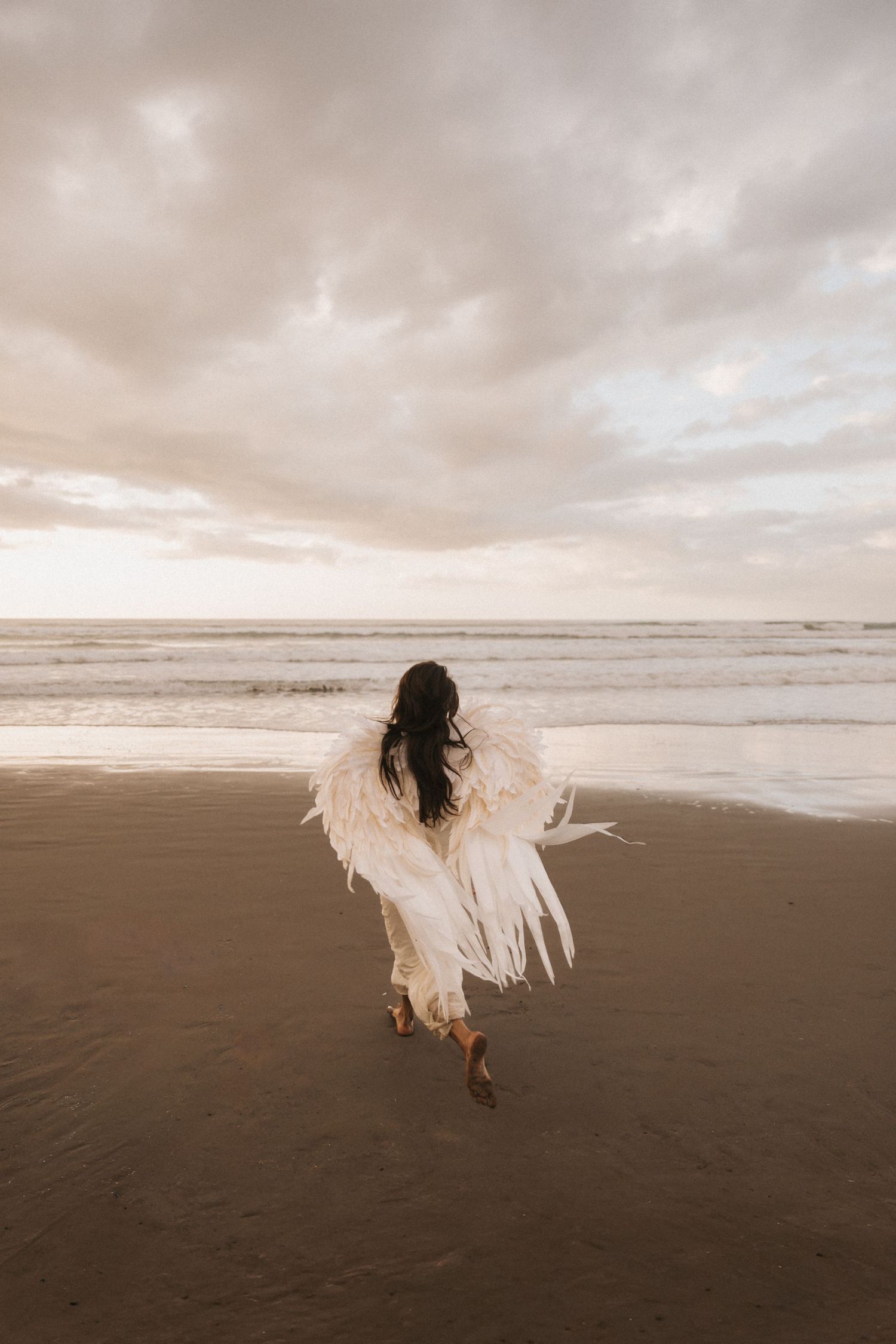 A figure in a flowing white dress runs along a misty beach shoreline at dusk creating an ethereal scene.