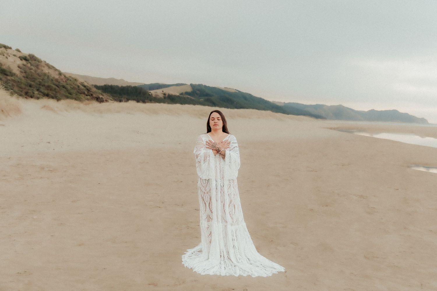 Elegant white lace dress photographed against serene beach landscape.