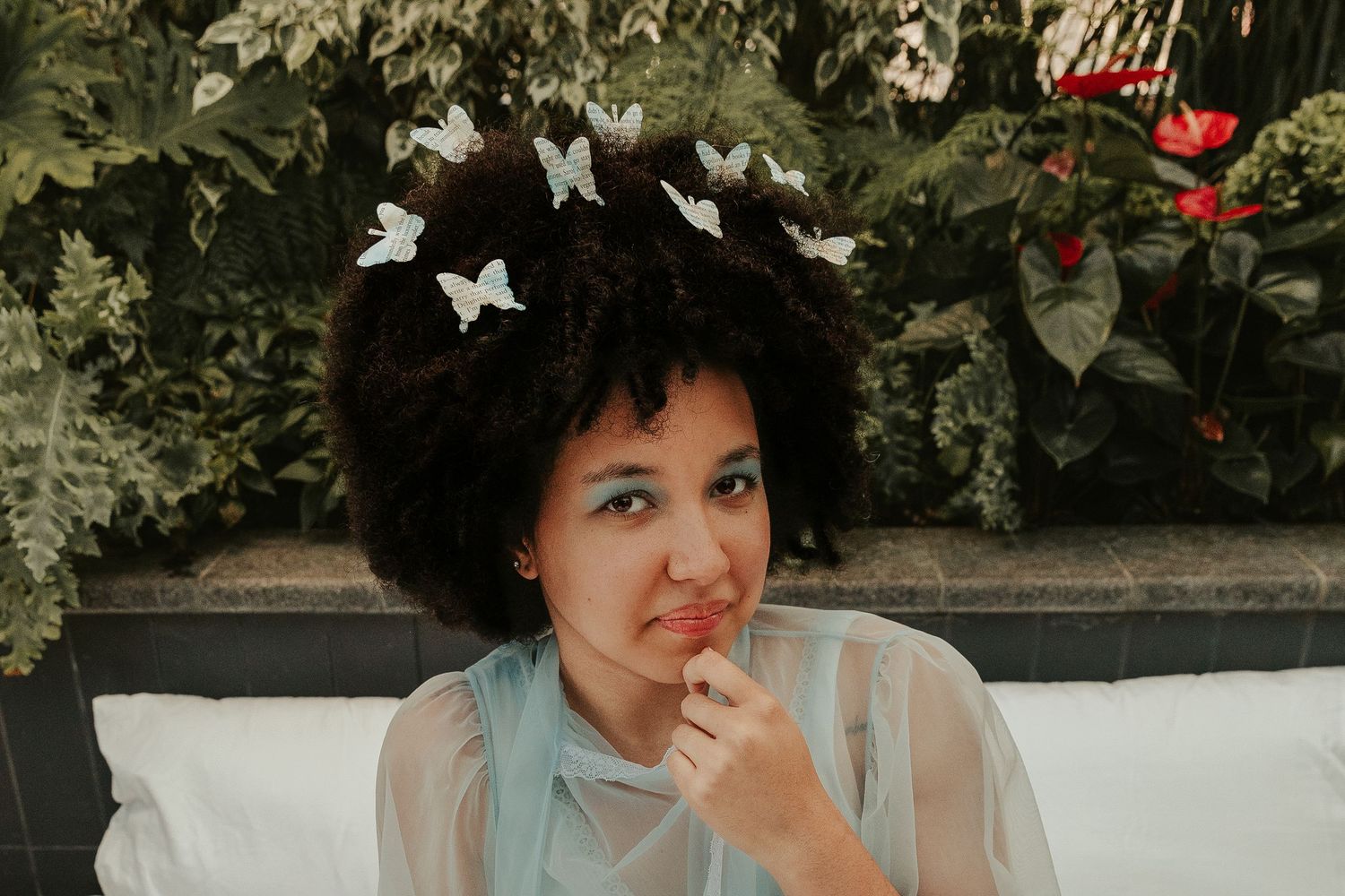 Person in light blue dress smiling while reading on white bedding with butterflies.