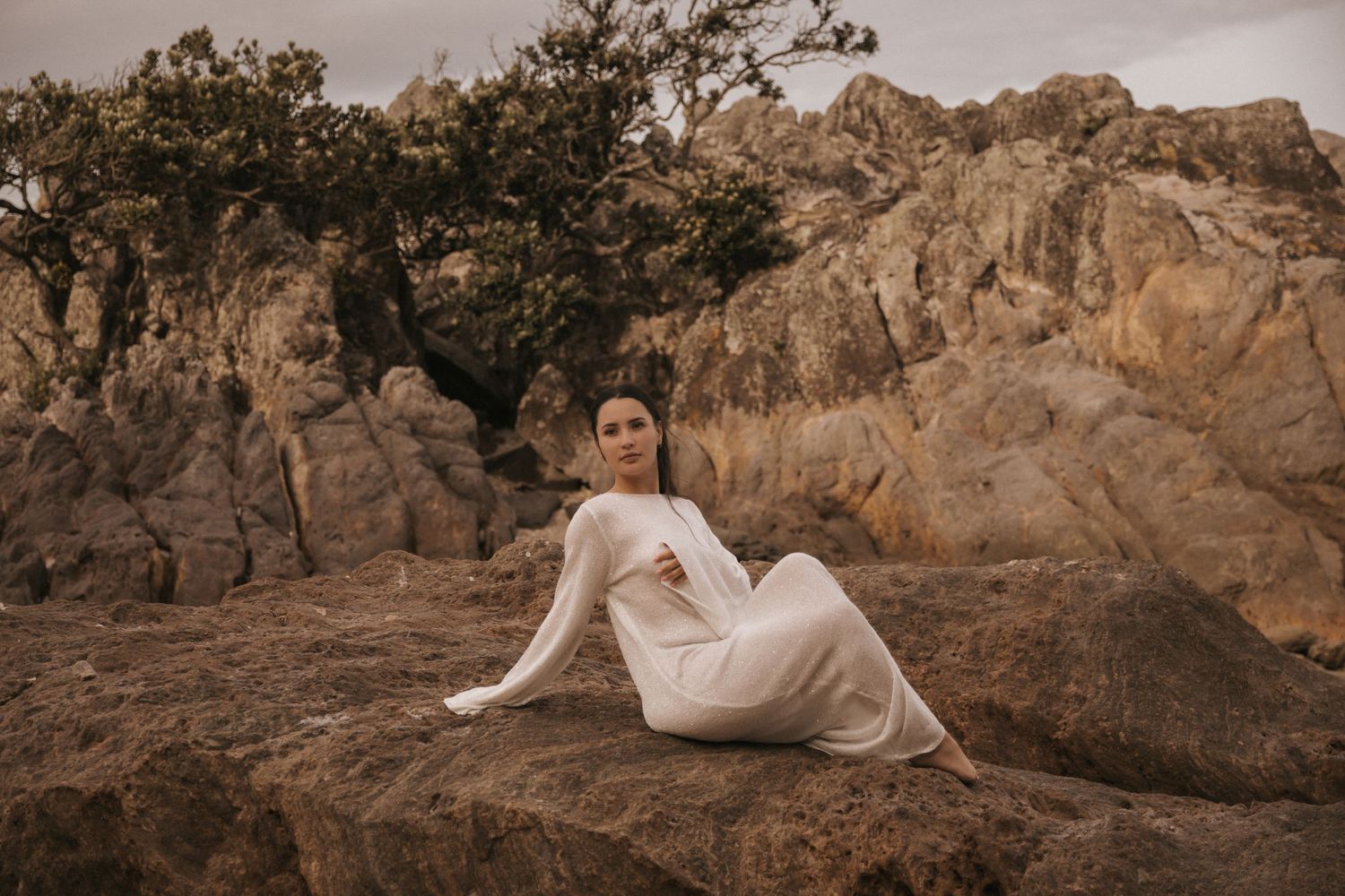 White dress photographed against rocky desert terrain in warm sepia tones.