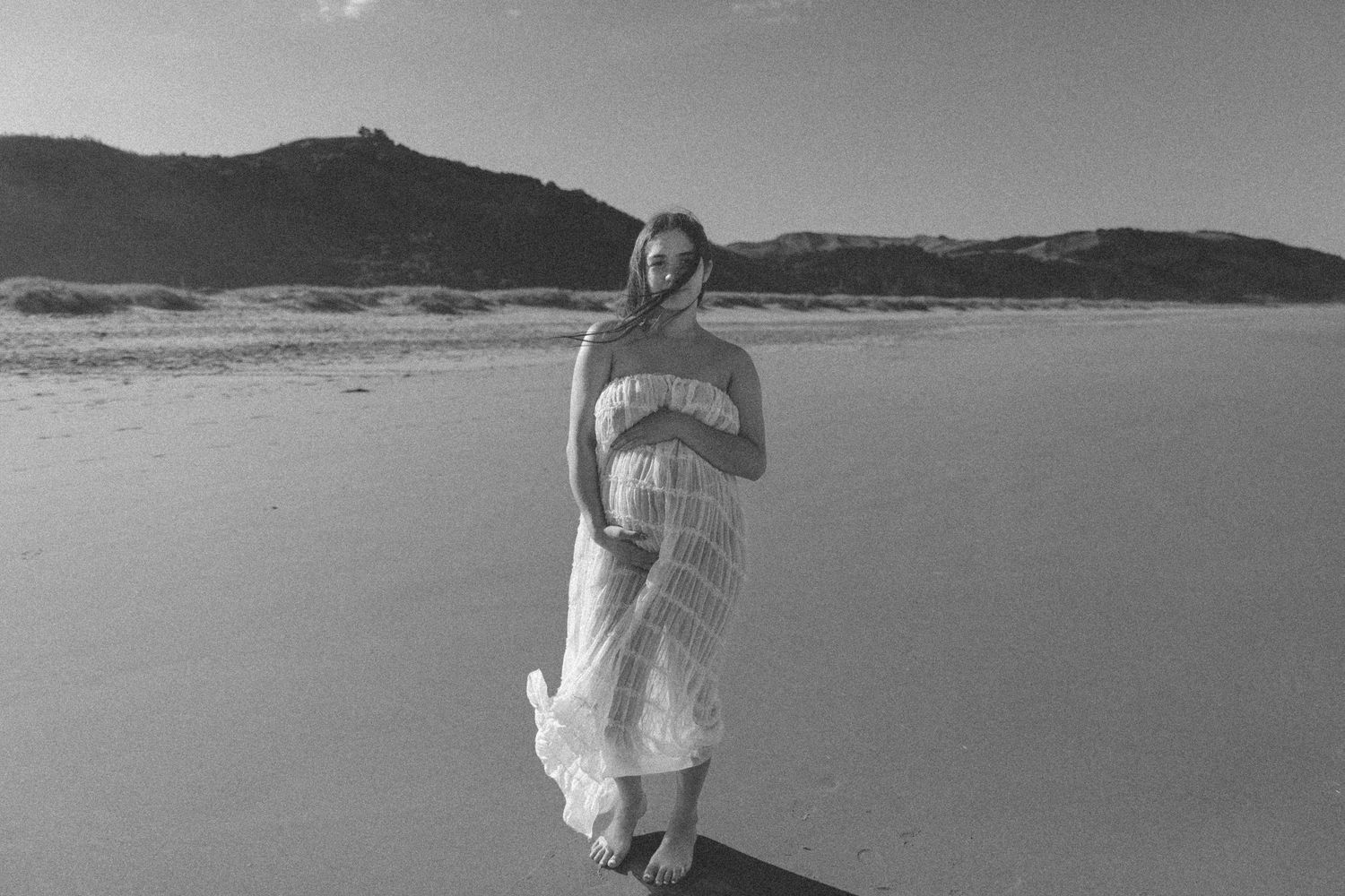 Black and white beach photoshoot with soft waves and mountains in background.