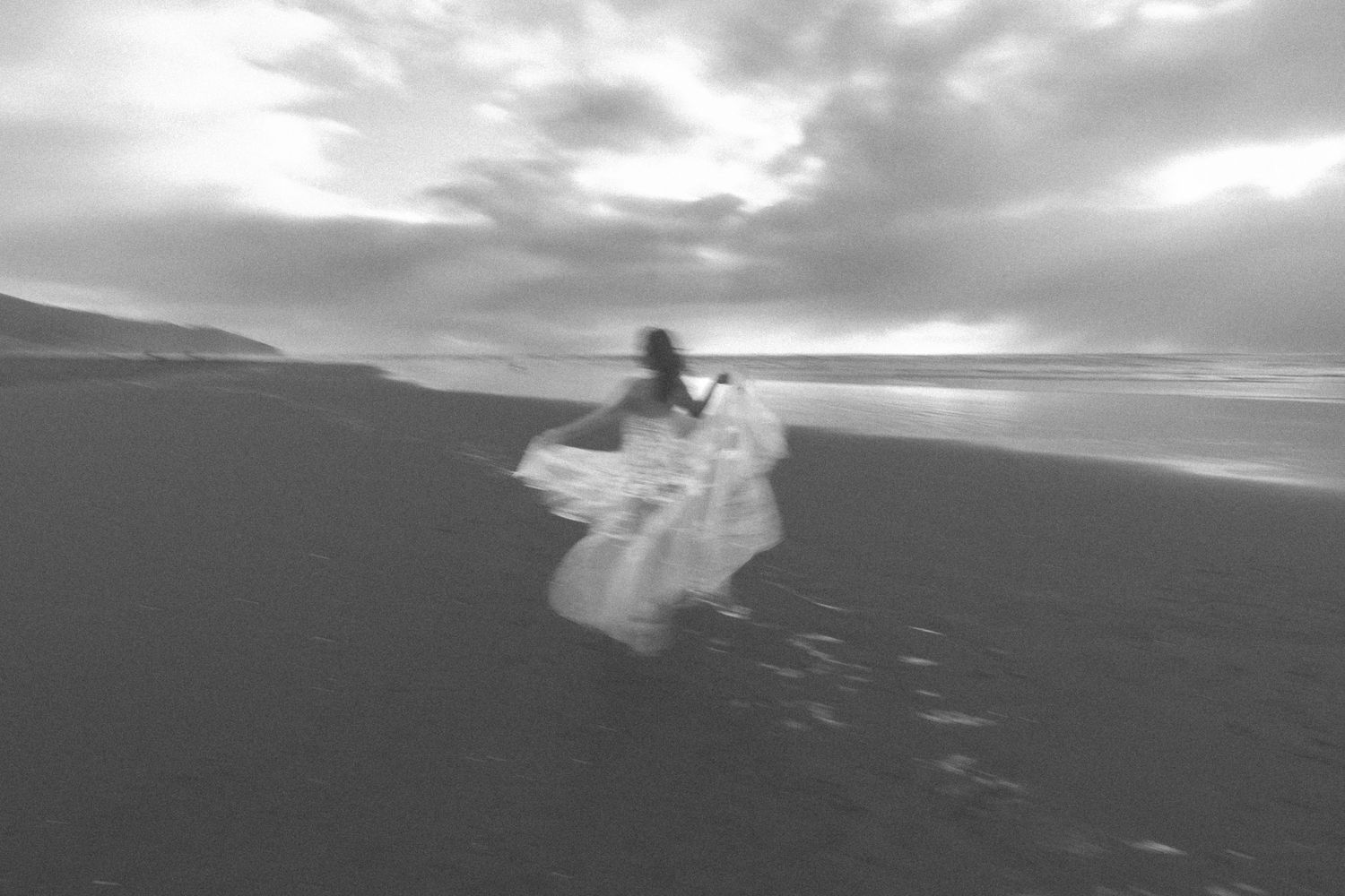 Silhouette of flowing white dress against moody coastal landscape.