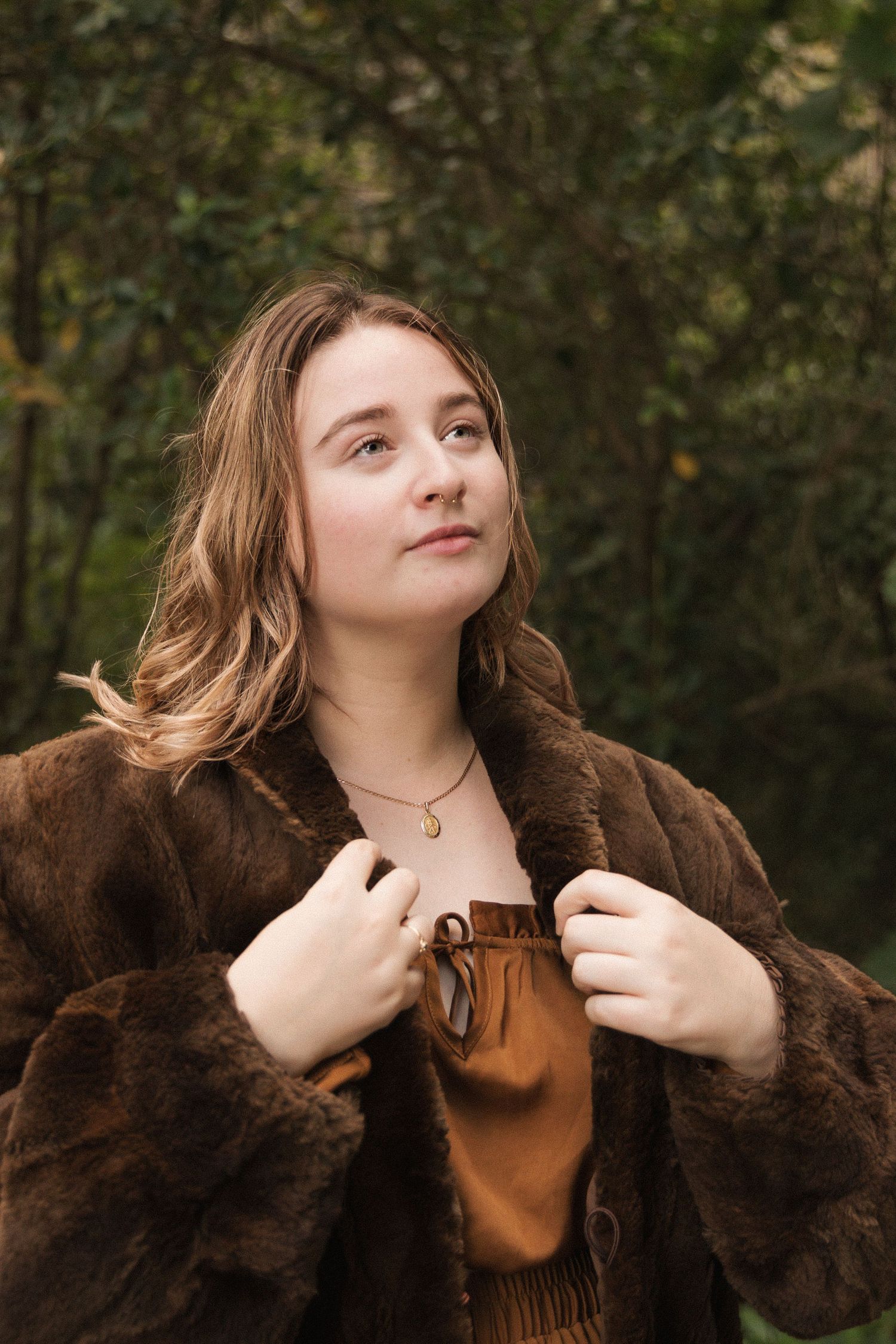 Stylish brown dress and fur coat ensemble captured against lush forest greenery.