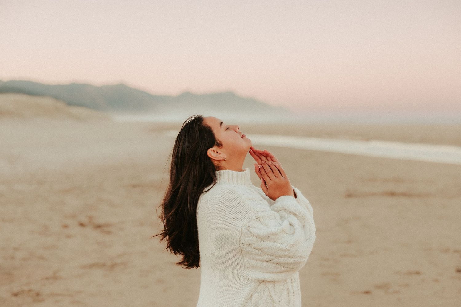 Silhouette twirling in white dress against pastel beach landscape.
