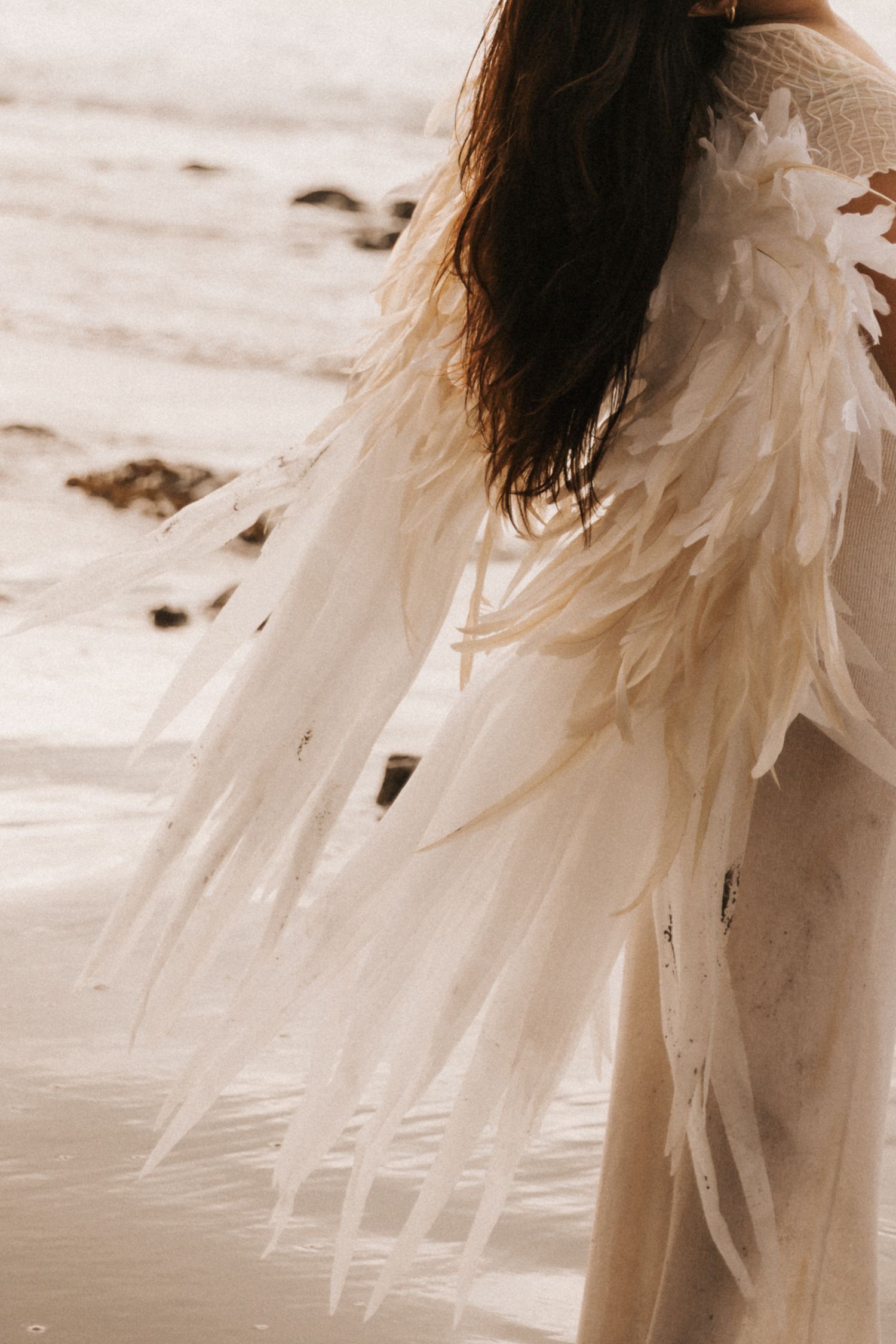 Ethereal white wedding dress with flowing fabric photographed in a soft sepia tone against a light background.