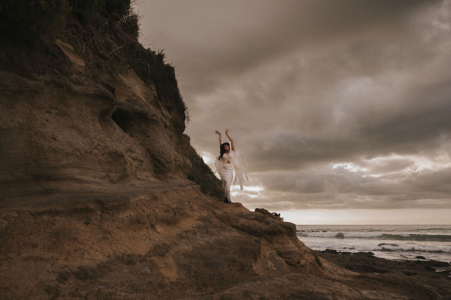 Dramatic aerial view of a rugged coastal cliff face with dark stormy clouds looming over the ocean.