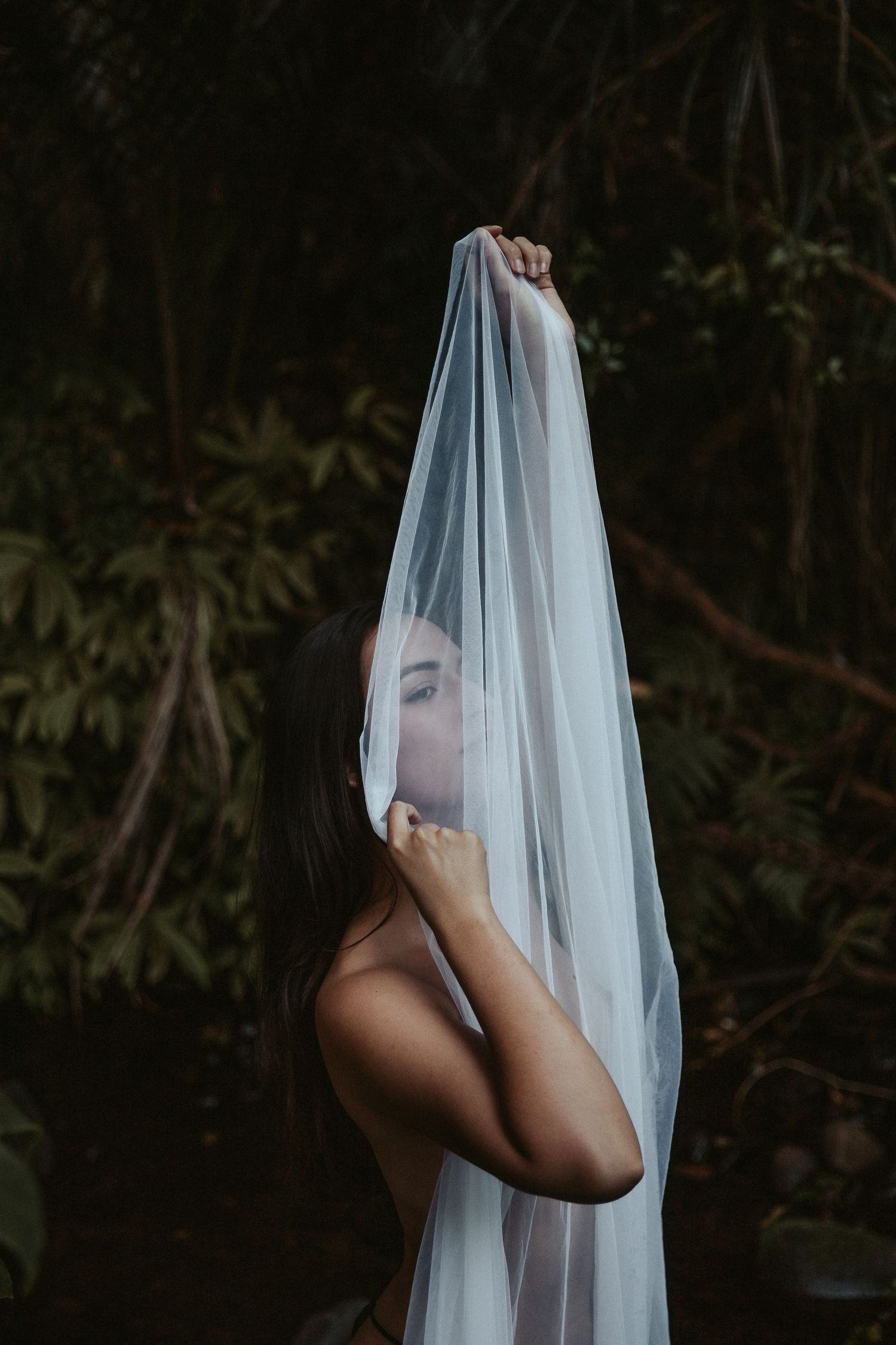 Artistic portrait with sheer fabric in moody garden setting.