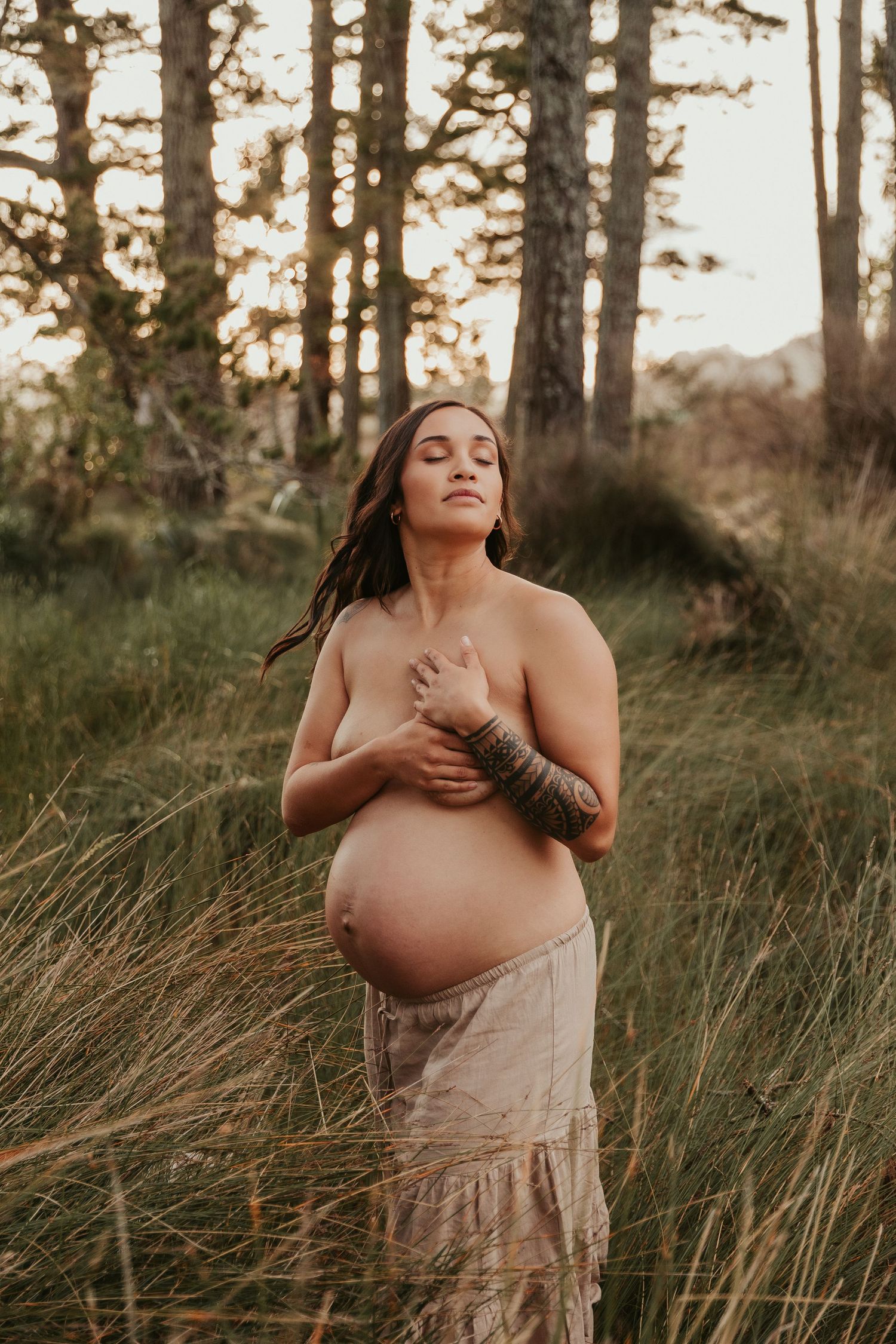 Sunset maternity photoshoot in a field of tall grass with golden hour lighting.