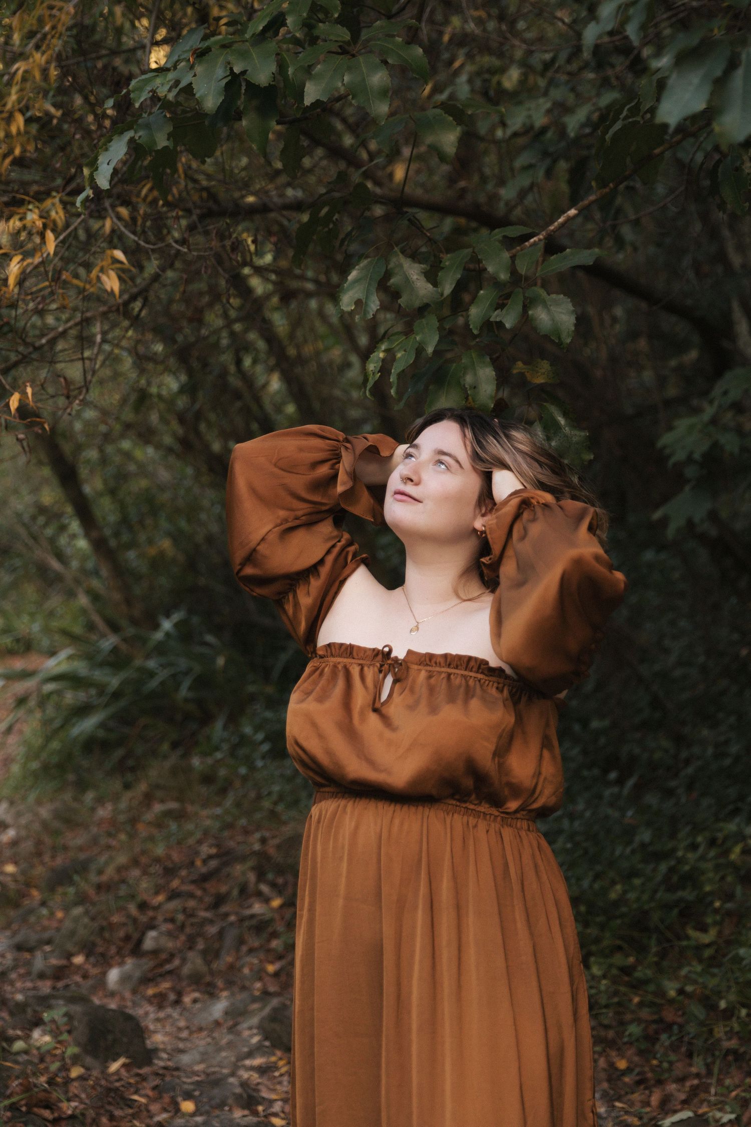 A flowing brown dress with dramatic sleeves captured in a moody woodland setting.