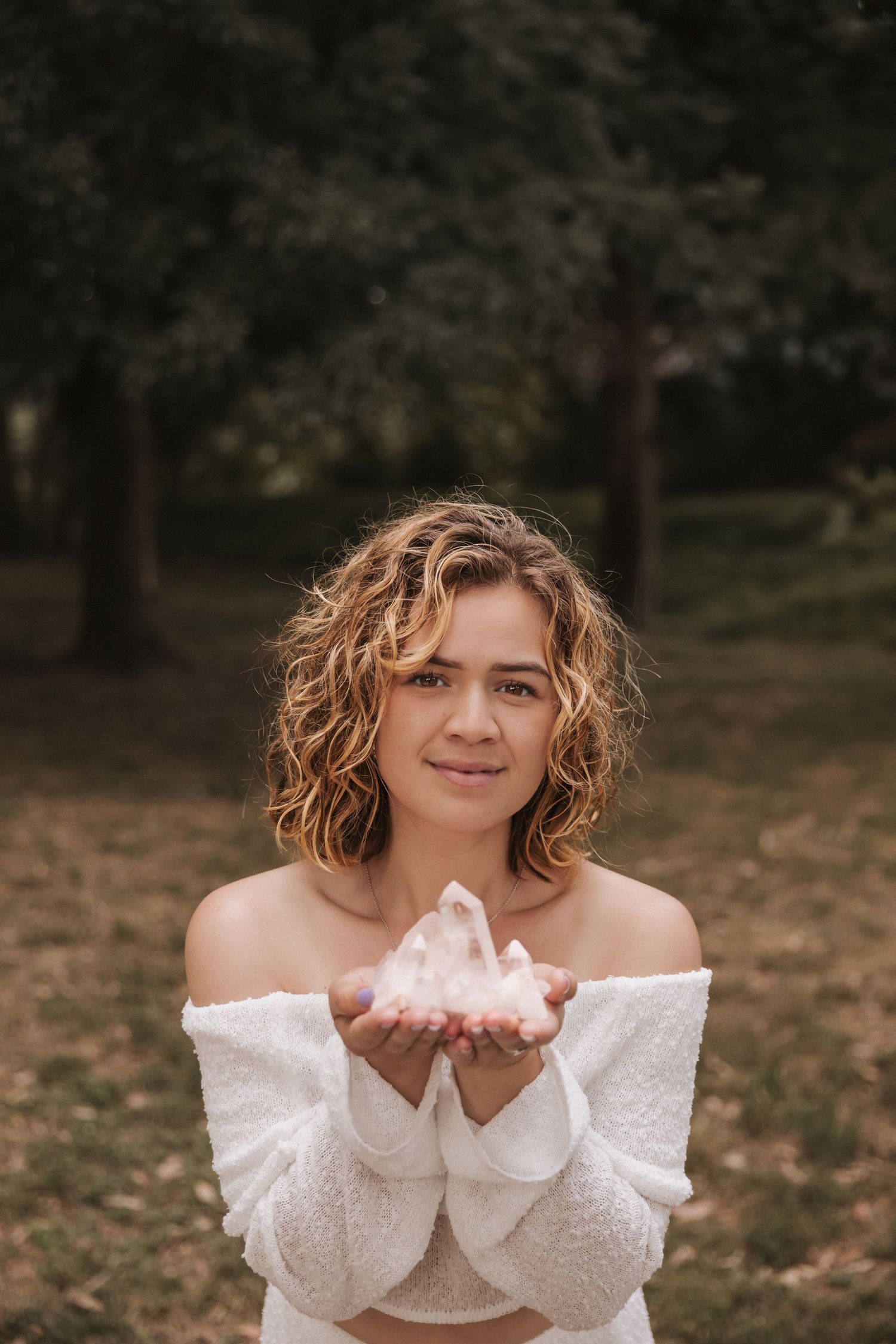 Woman in white off-shoulder dress holds something in cupped hands outdoors.
