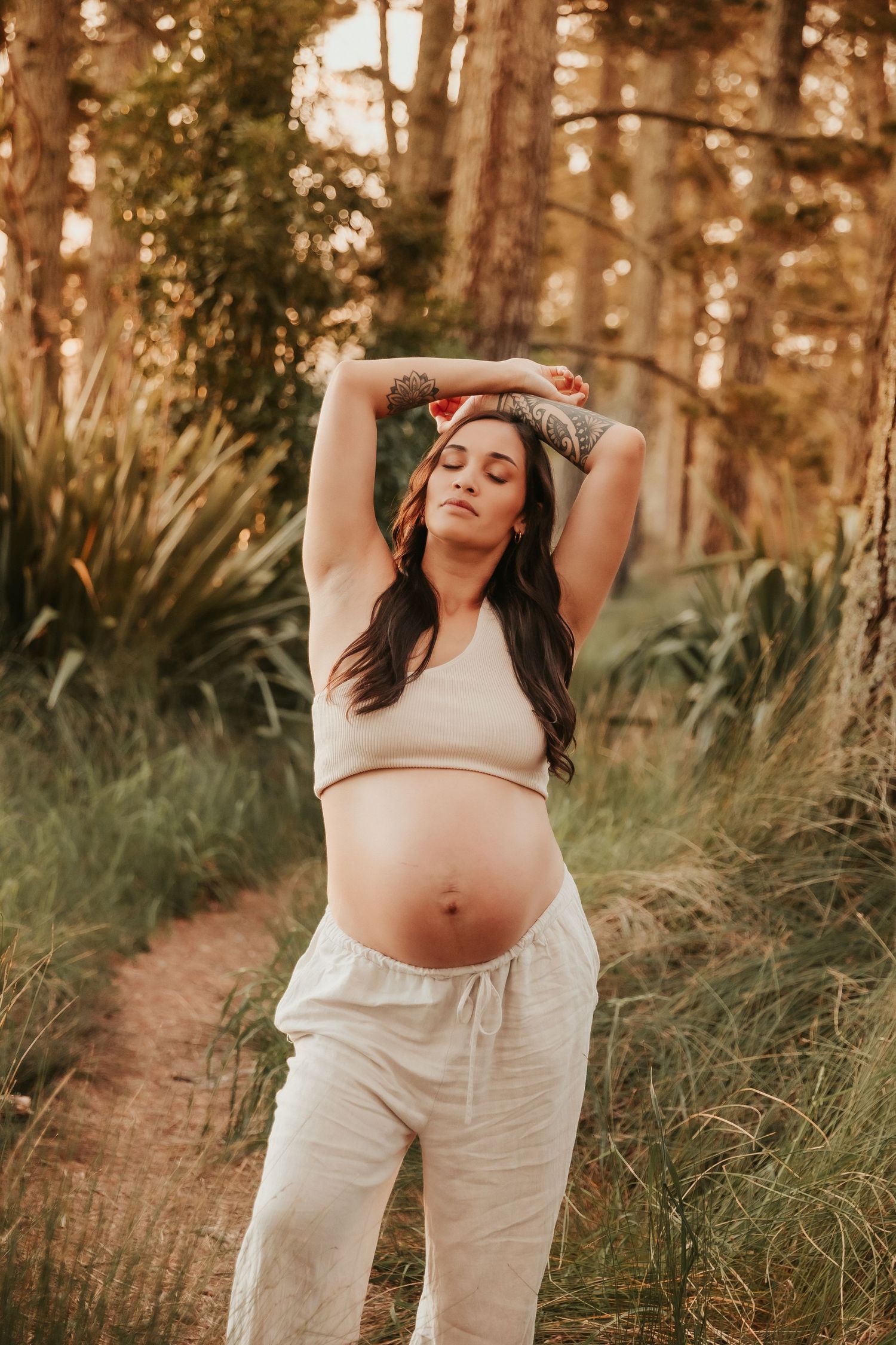 Maternity photoshoot in forest setting with sunlight filtering through pine trees.