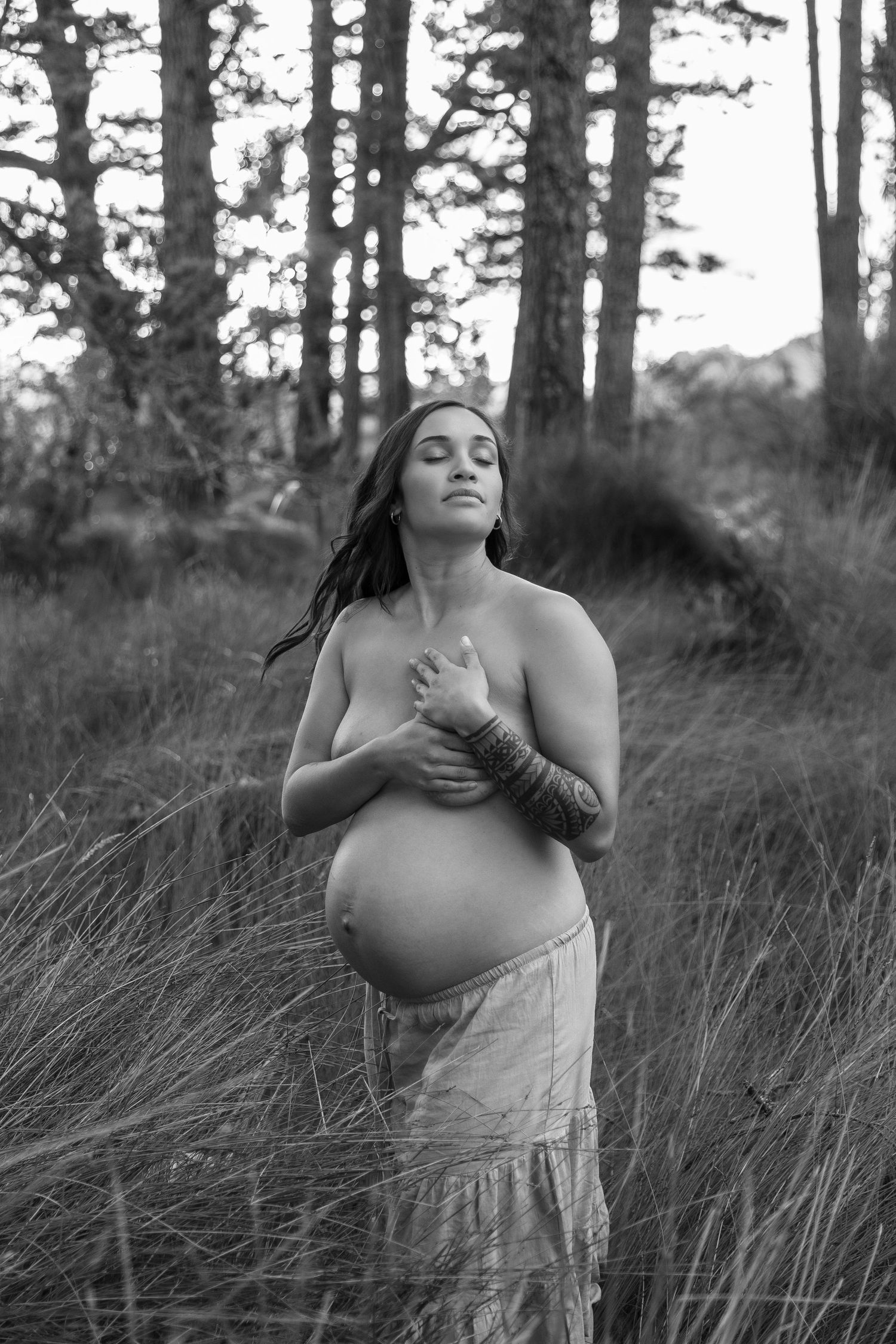 Black and white maternity portrait in a forest setting with tall grass and pine trees.