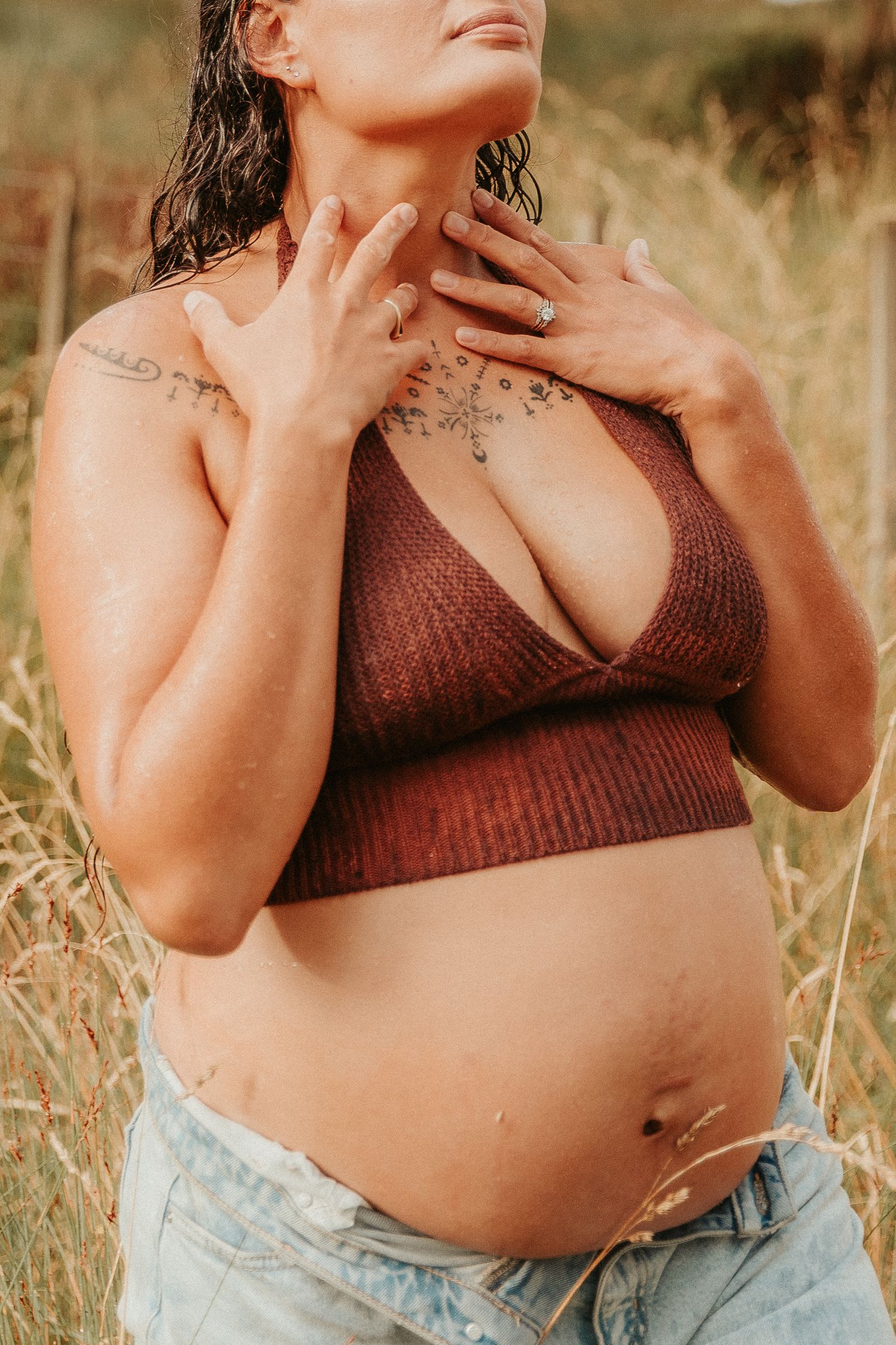 Person wearing a brown knit top poses against a natural outdoor backdrop with dried grass.