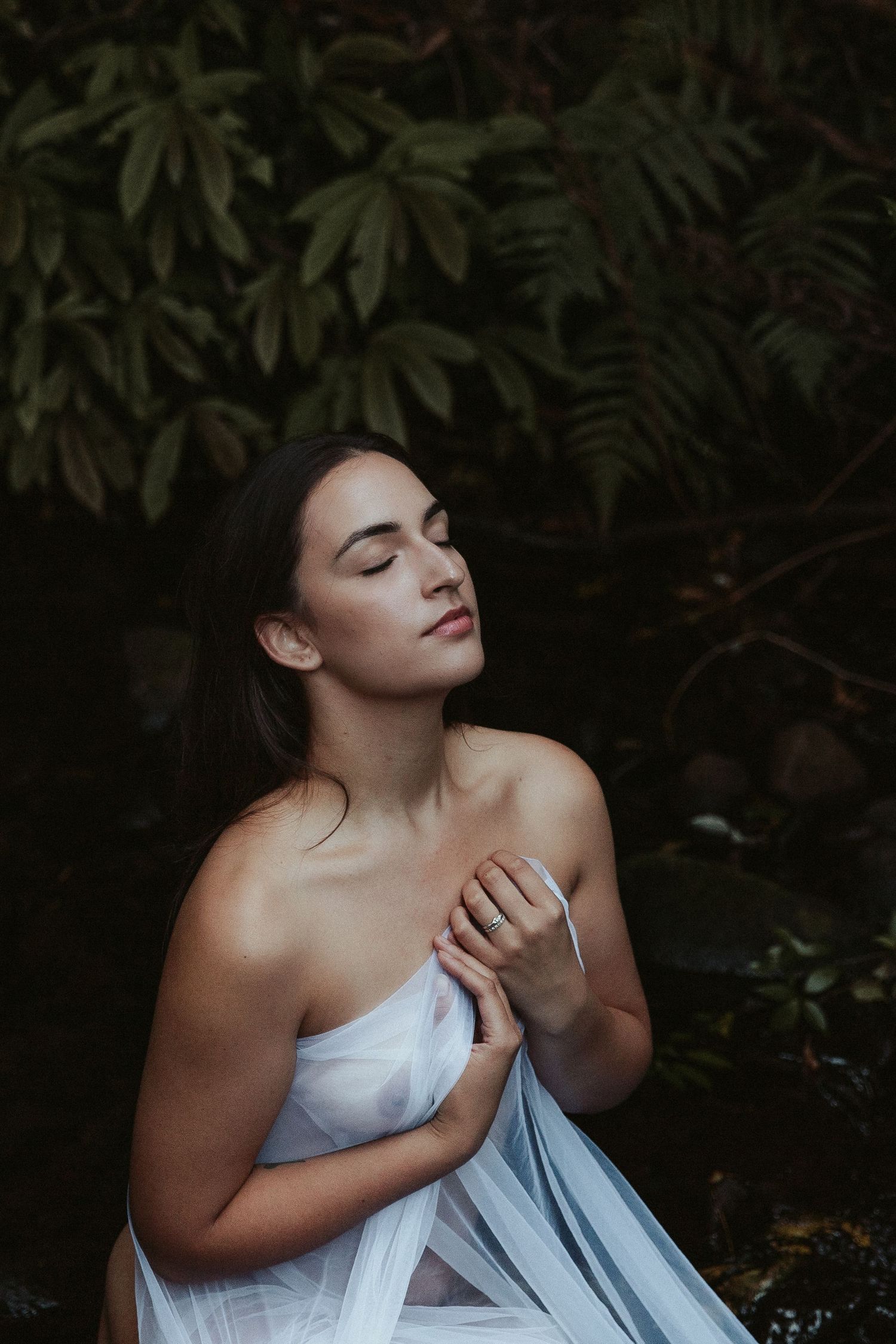 Dramatic portrait in white dress against dark foliage background.