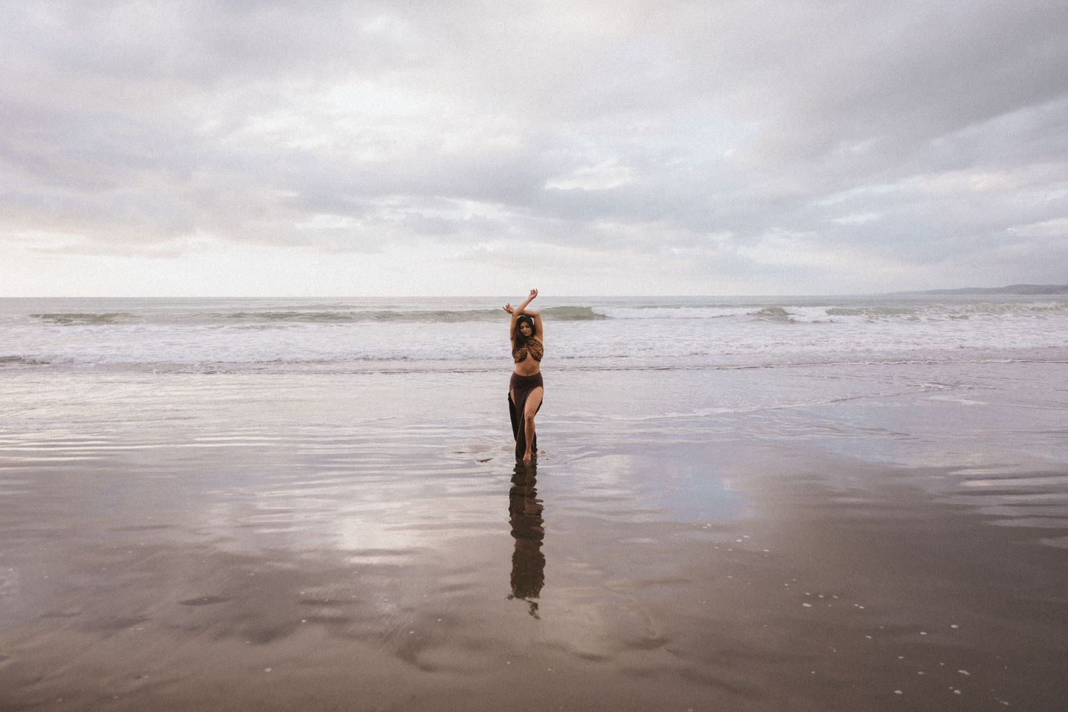 A person walks along a misty beach shoreline with waves crashing in the background on an overcast day.