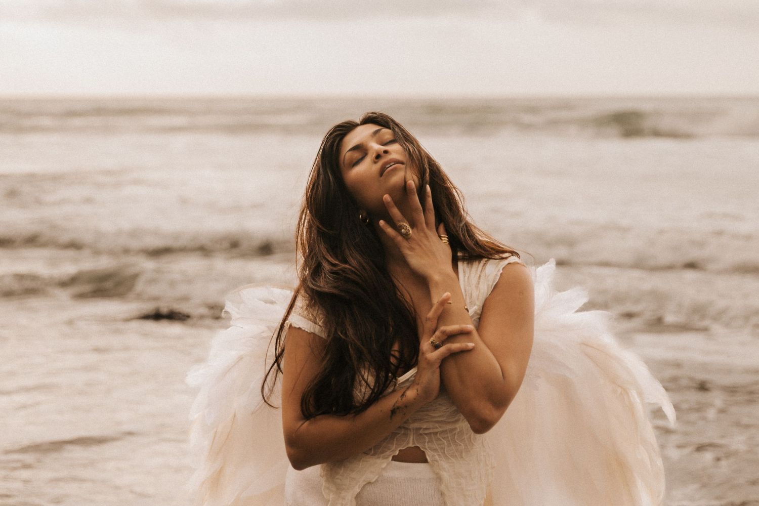 A romantic beach photoshoot featuring a couple in wedding attire embracing by the ocean waves at sunset.