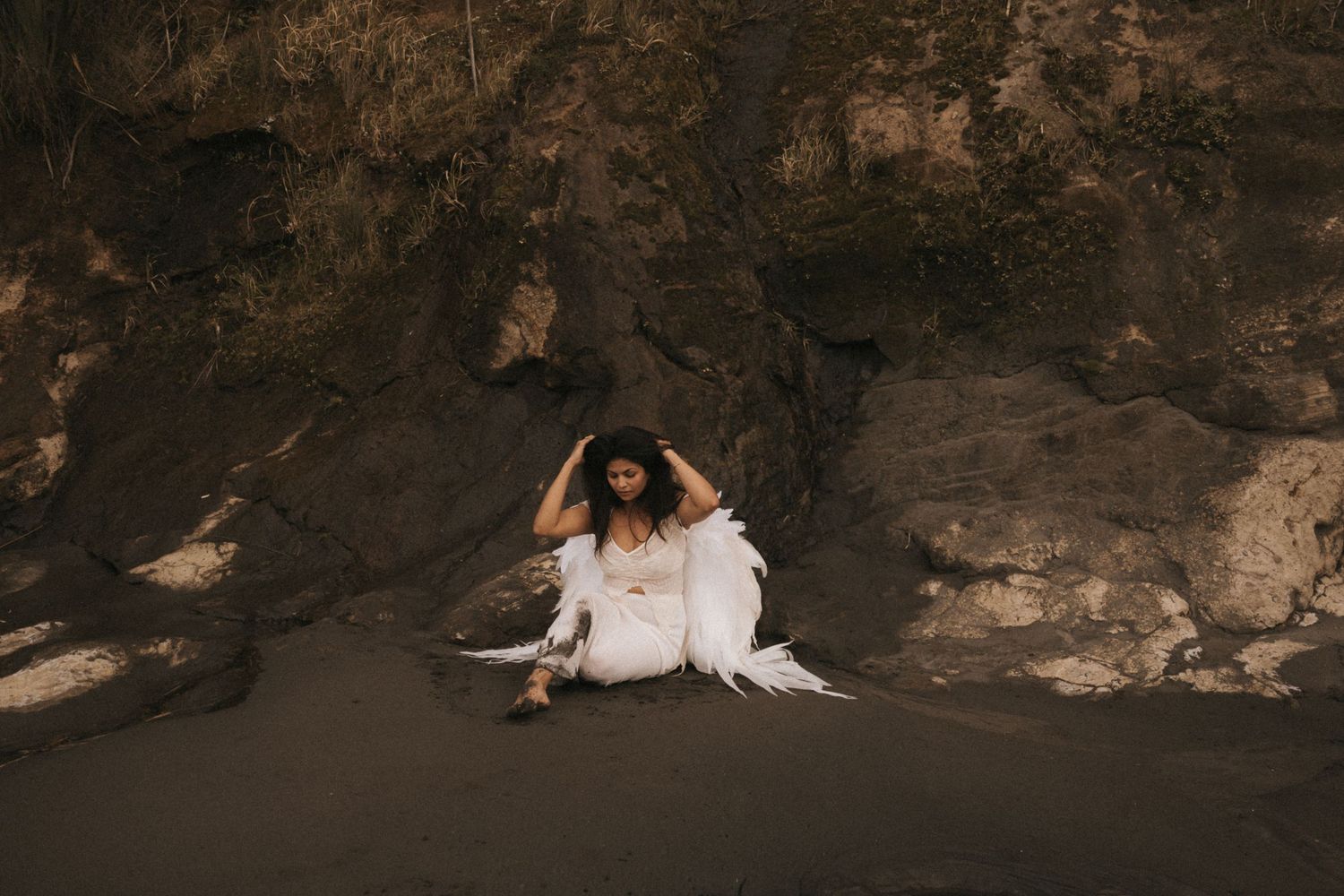 A small white dog lies on a rocky cave floor near natural stone formations.