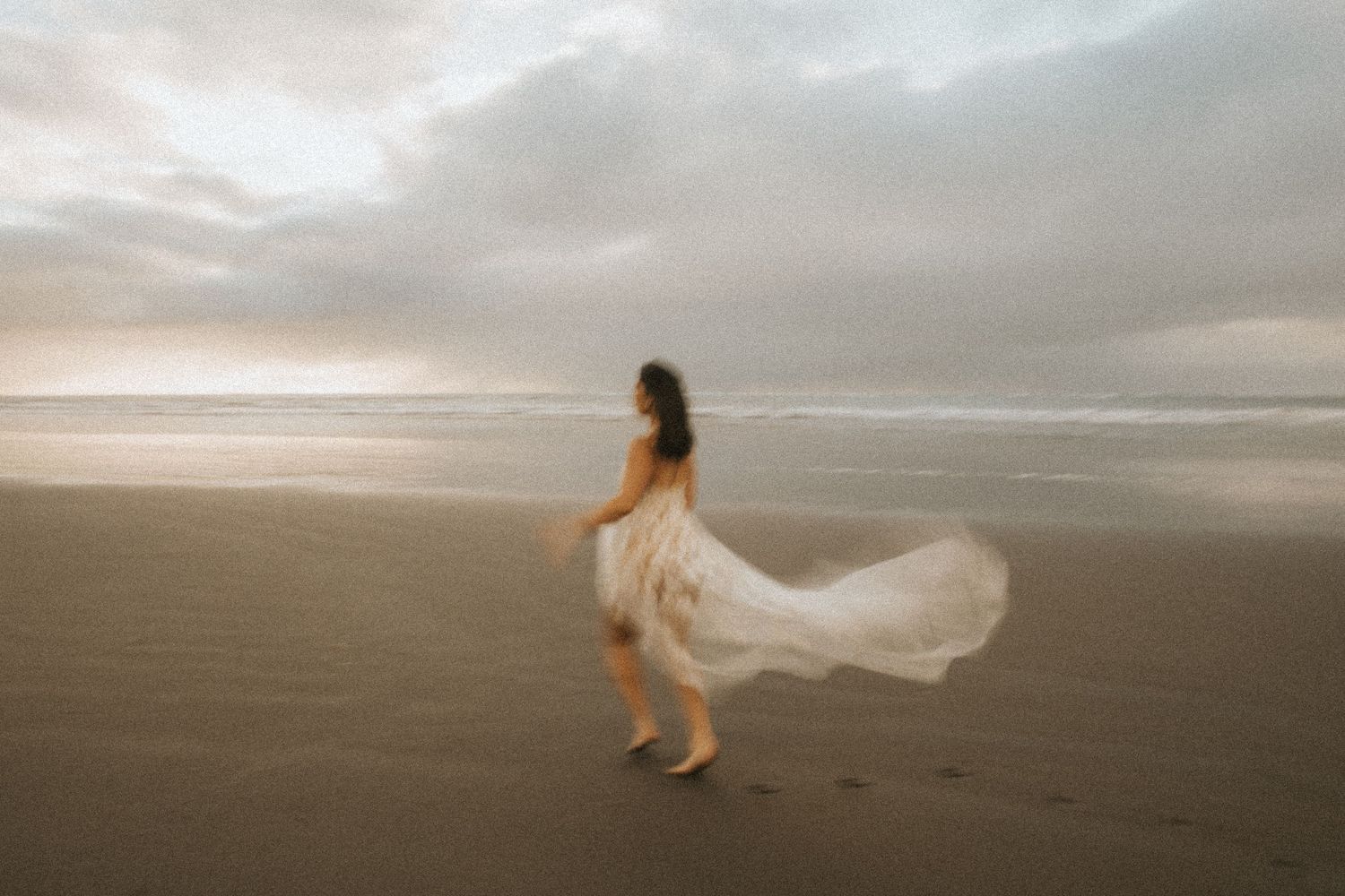 A white flowing dress moves gracefully against a moody beach landscape.
