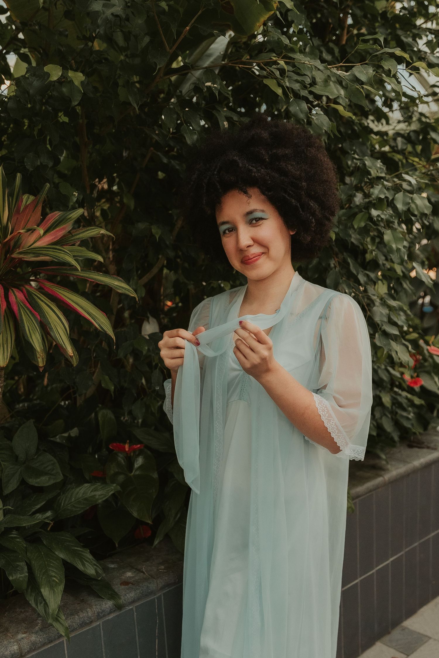 Whimsical outdoor portrait session in pale blue dress among garden foliage.
