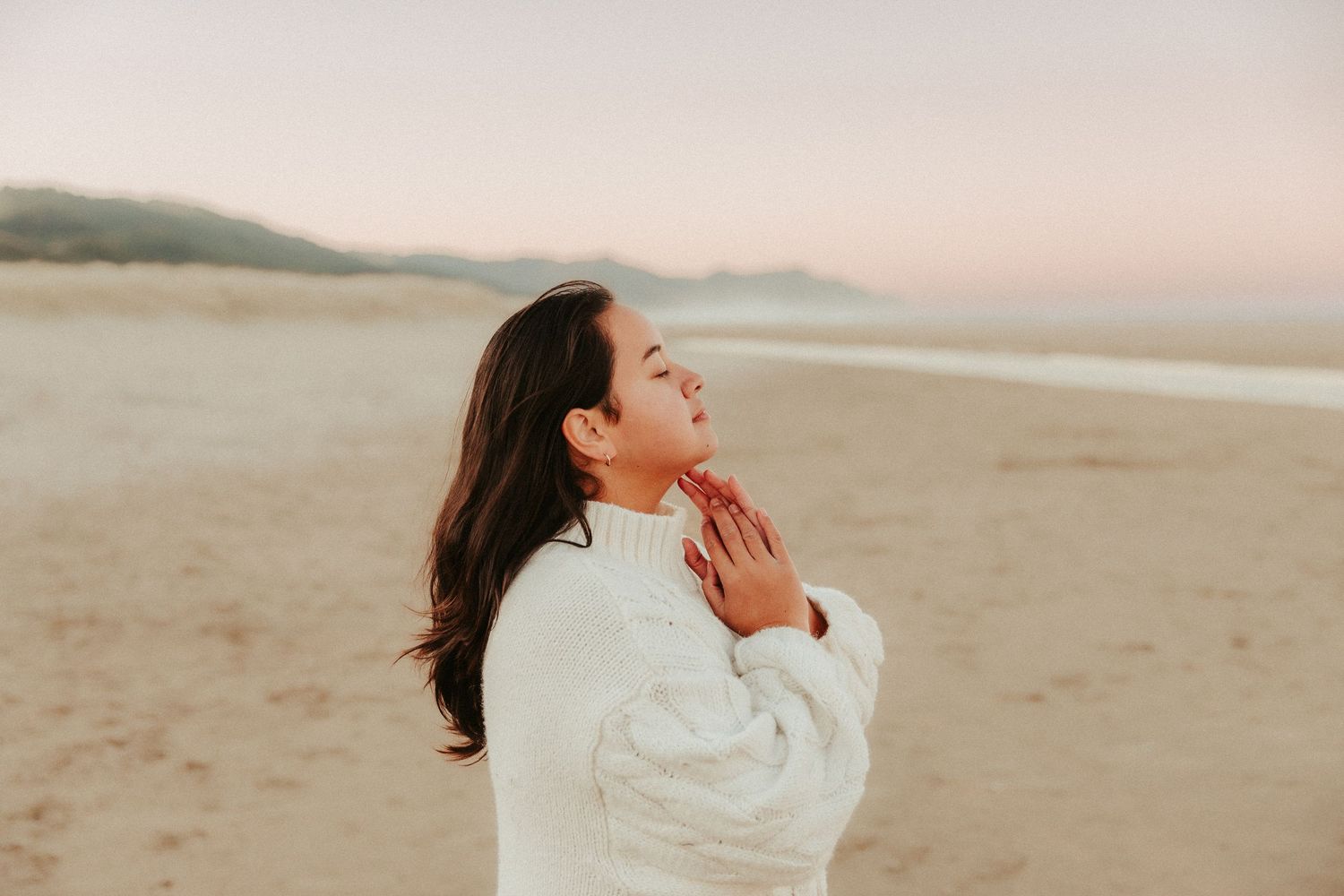 Figure in white clothing moving gracefully on sandy beach at dusk.