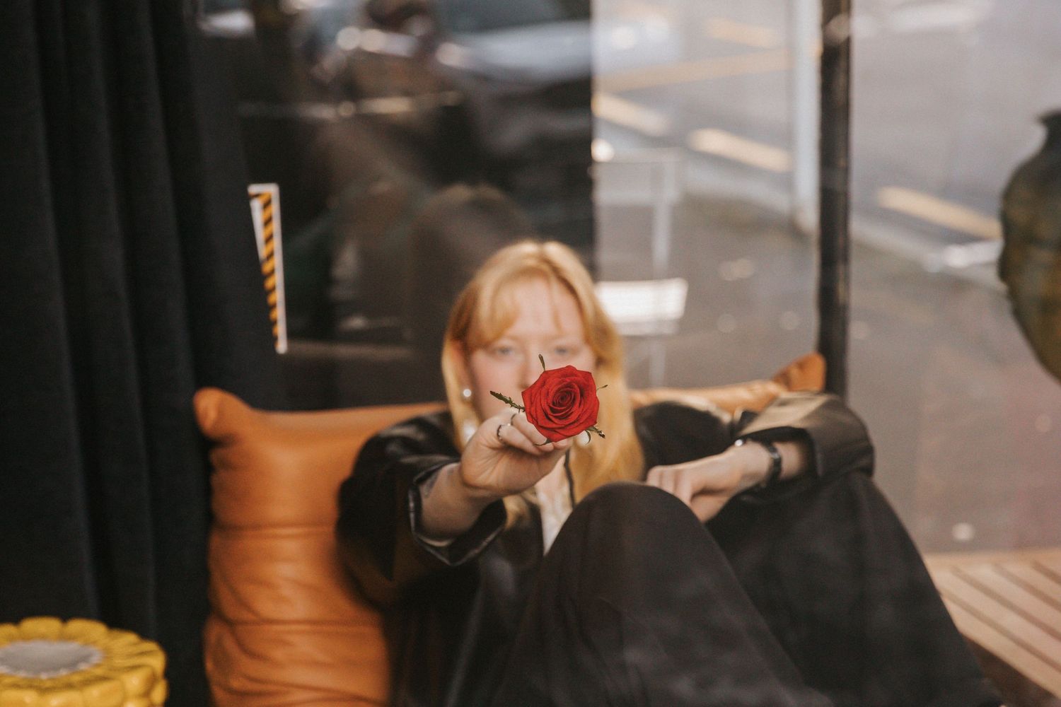 Someone holds up a red rose while sitting near a window in a dimly lit cafe setting.