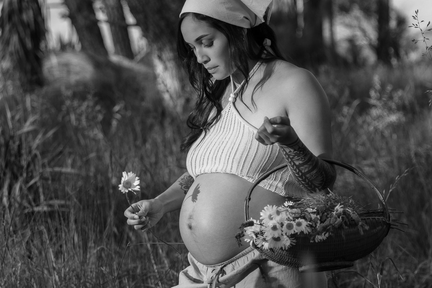 A series of black and white maternity photos showing a pregnant woman holding flowers in an outdoor garden setting.