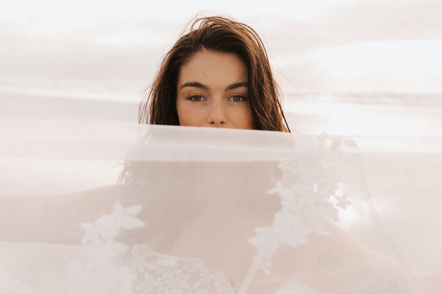 Minimalist beach portrait with soft lighting and ethereal white fabric.