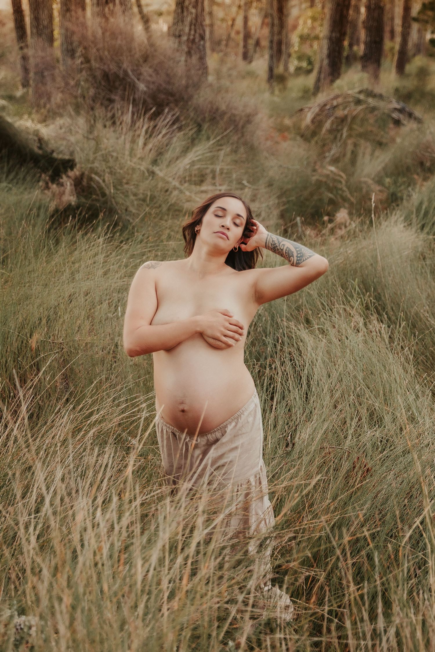 Natural light maternity session among wild grasses with warm sunset tones.