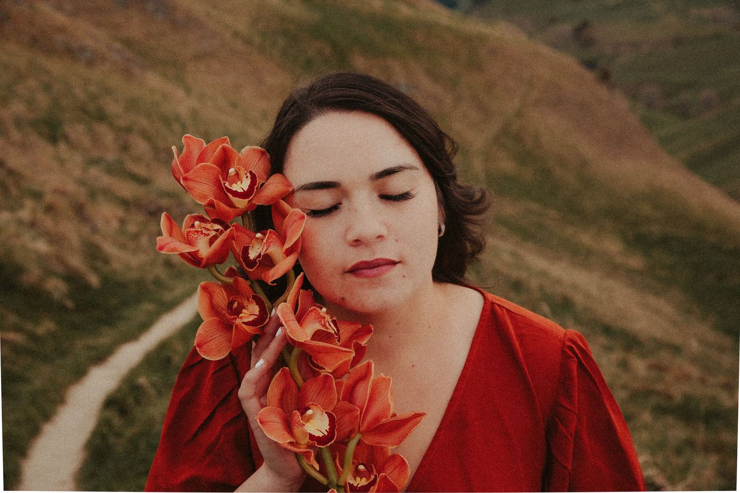 Romantic portrait with vibrant coral flowers against a mountainous landscape.