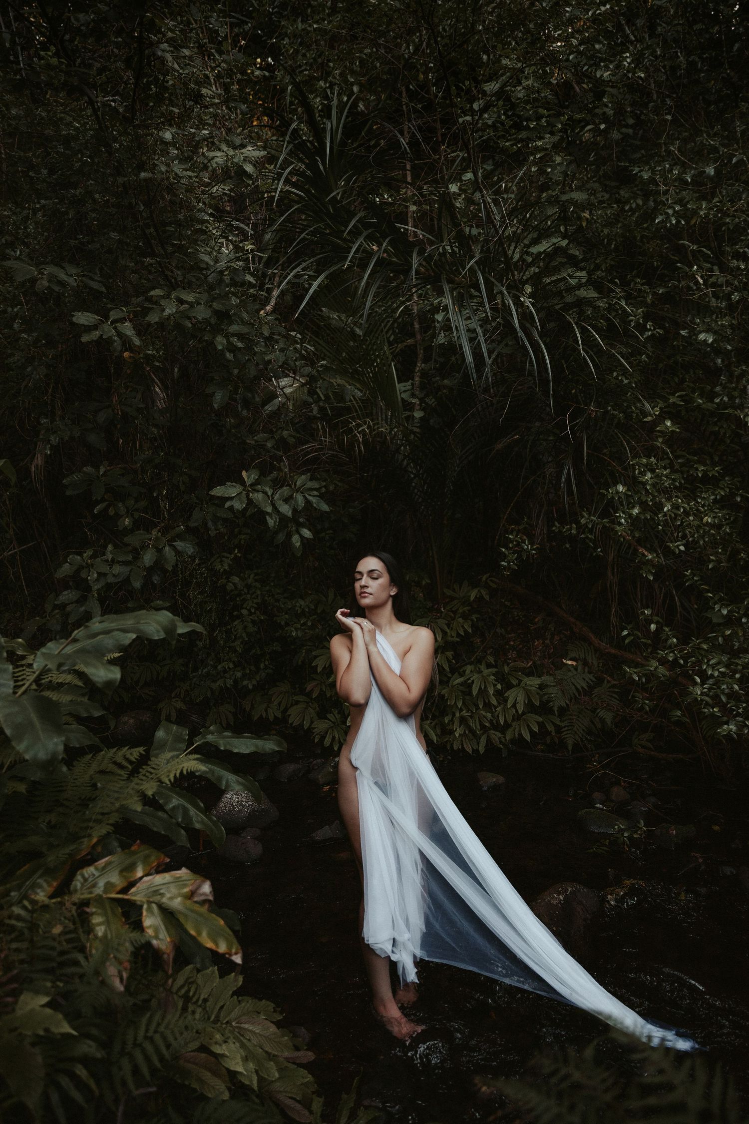 Artistic portrait with flowing white fabric creating movement against dark forest background.