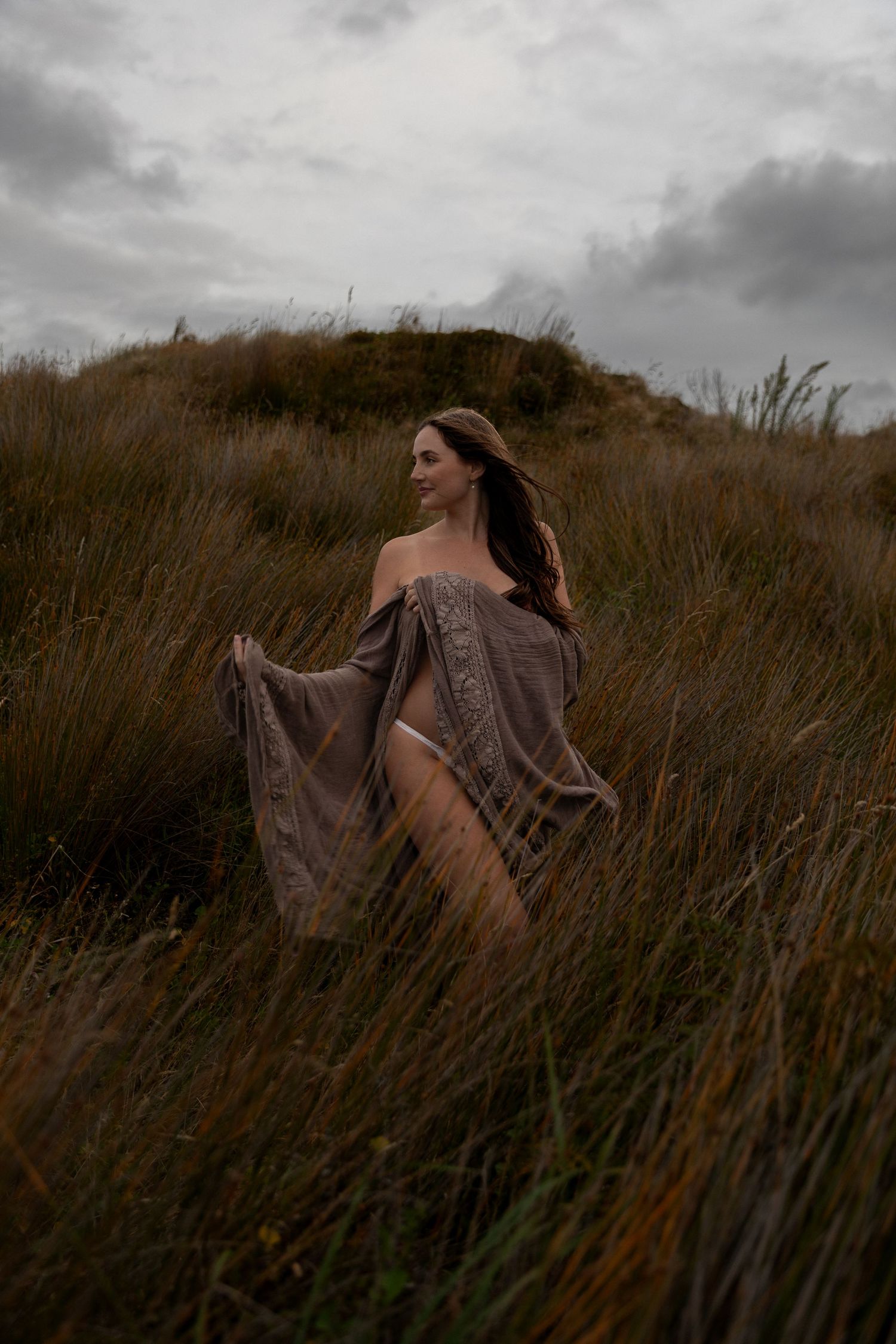 Moody landscape portrait in tall grass field with cloudy sky background.