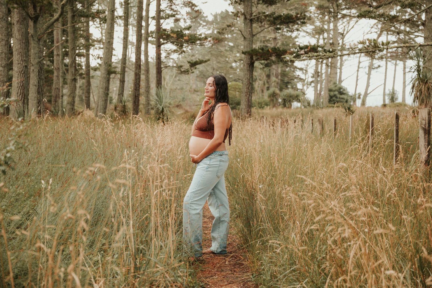 Figure walks through tall grass with pine trees creating a serene forest backdrop.