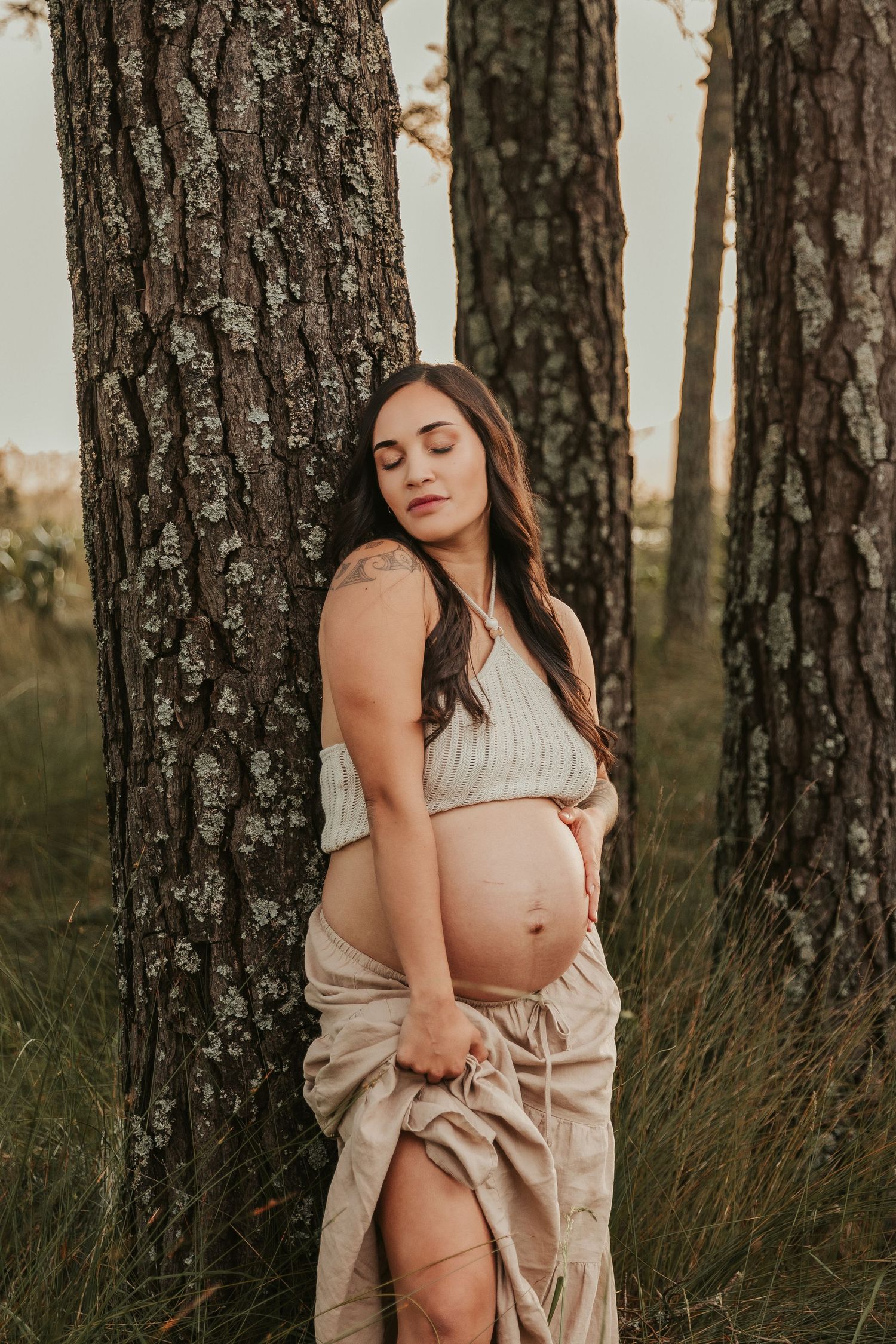 Artistic portrait in a forest setting with soft beige tones and tall pine trees.