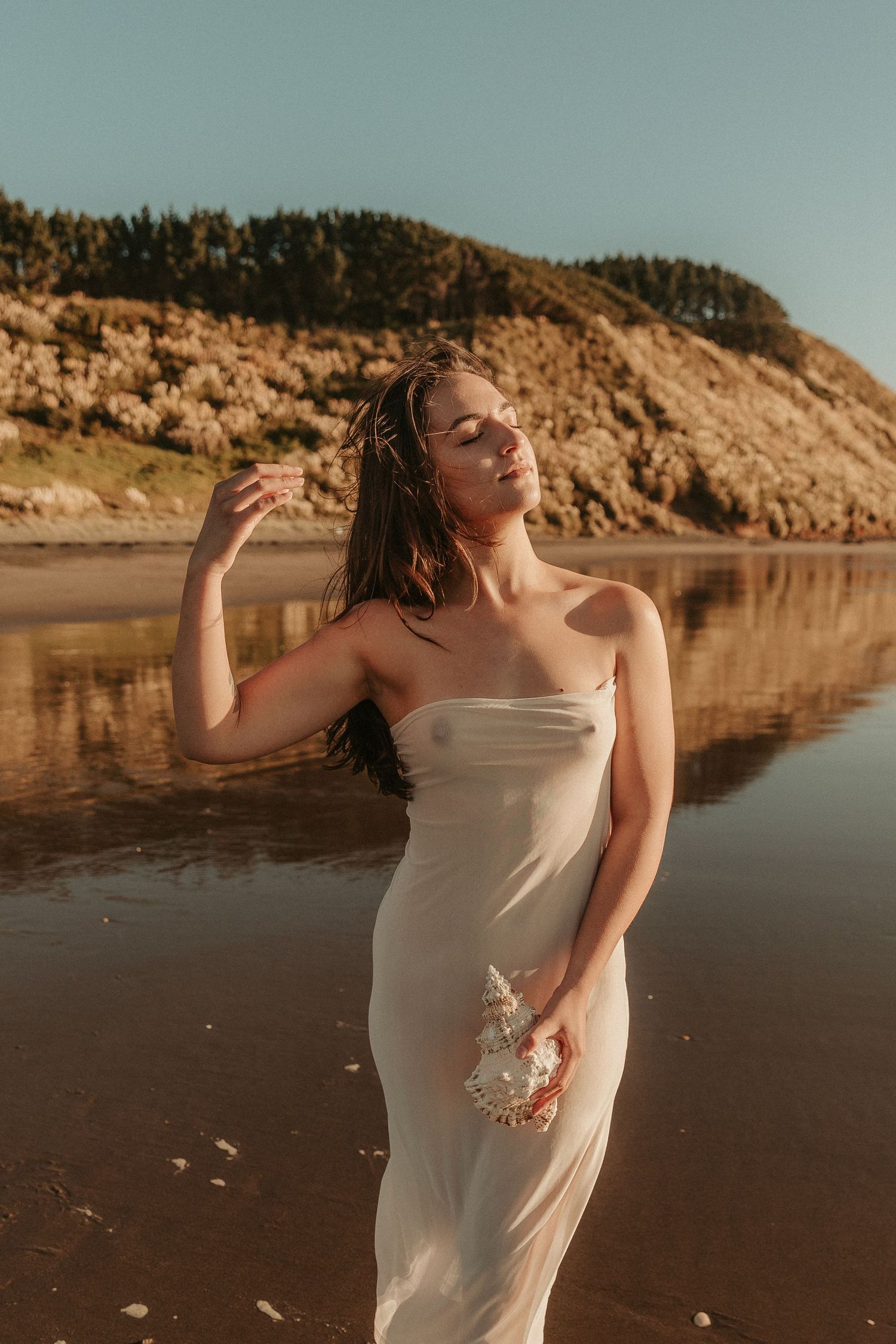 Artistic maternity photography at a beach with rocky cliffs and serene water backdrop.
