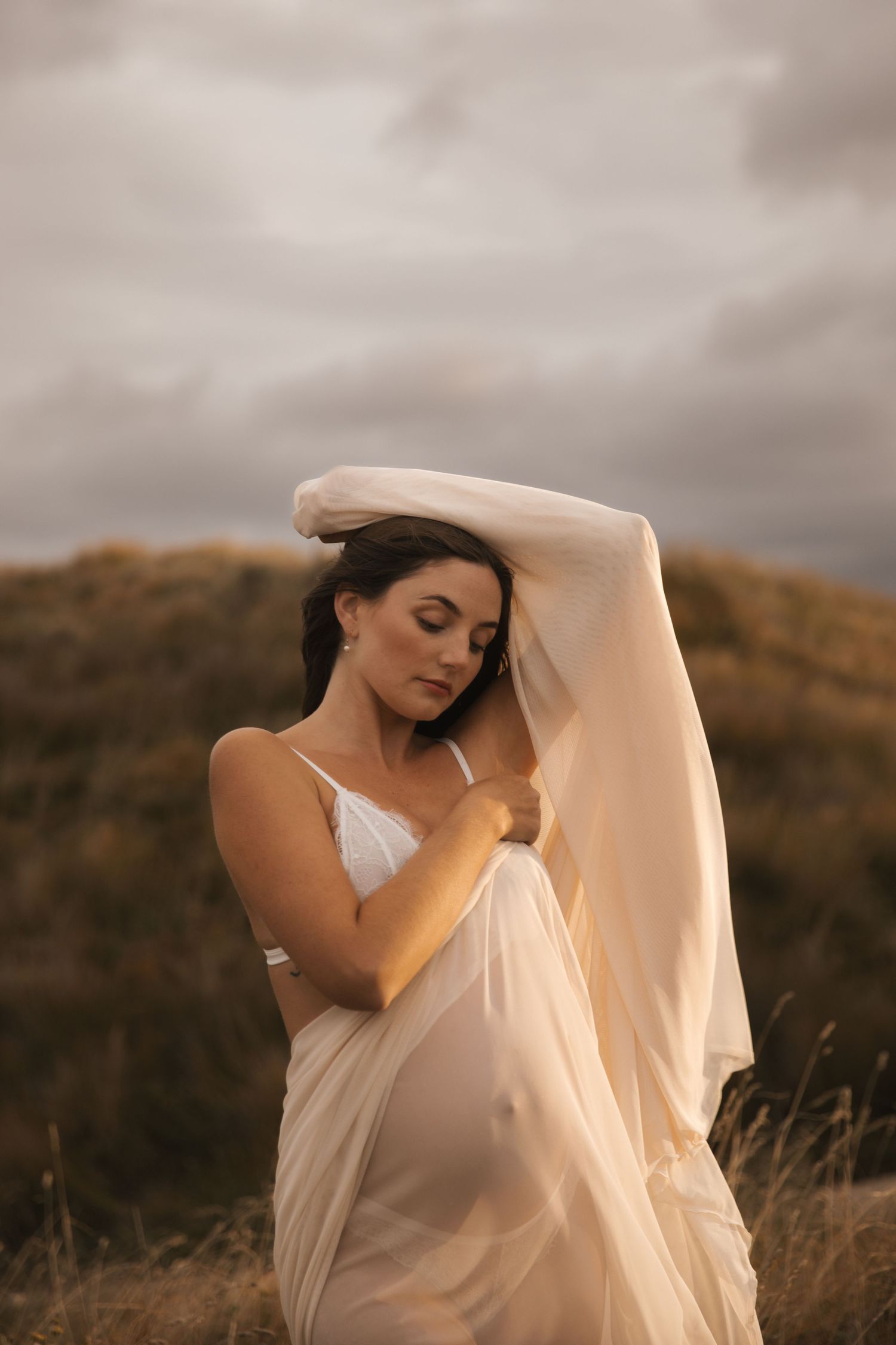 Soft, romantic maternity portrait with flowing white fabric at golden hour.