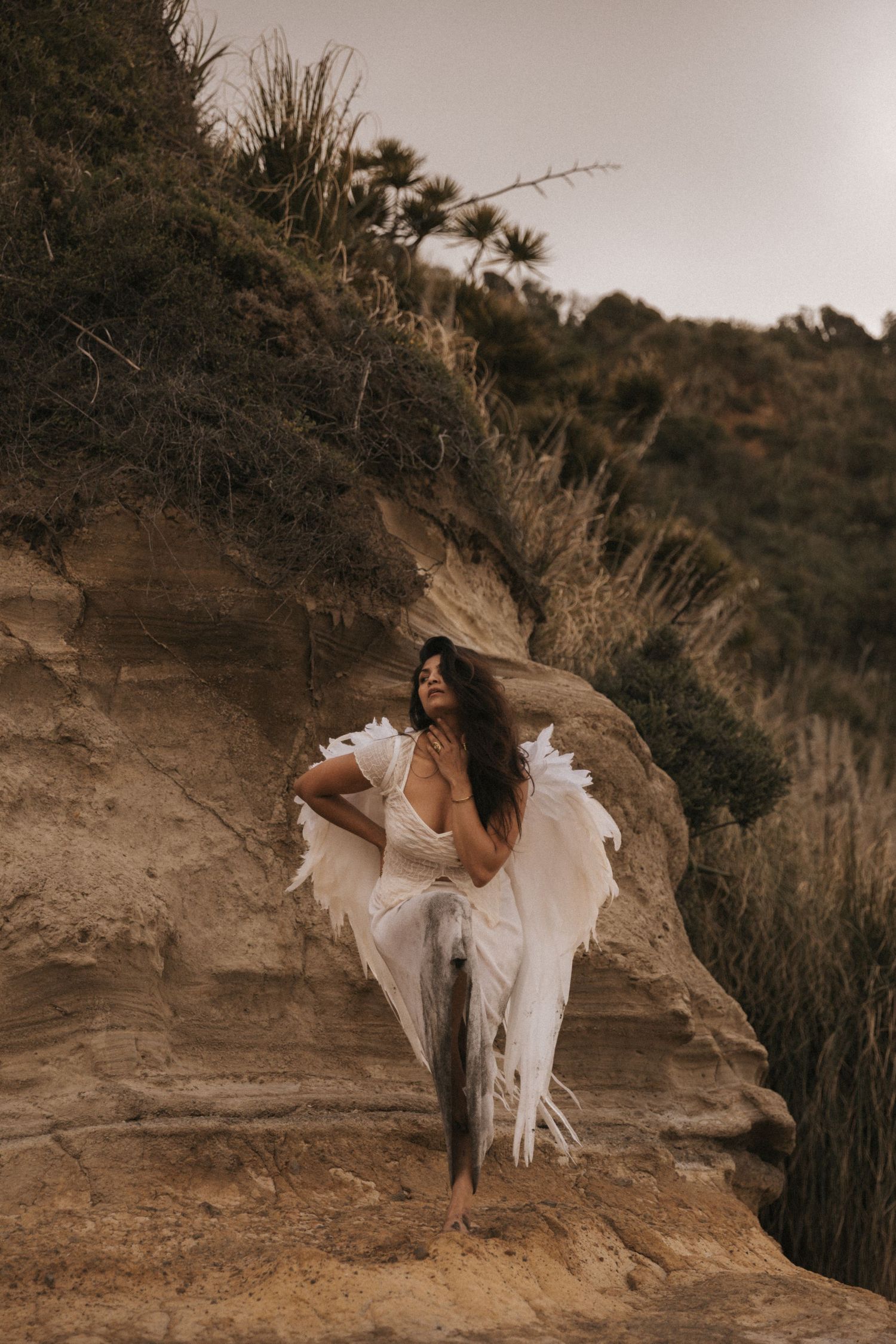 A figure in a flowing white dress poses gracefully on a rocky cliff edge at sunset creating a dreamy atmosphere.