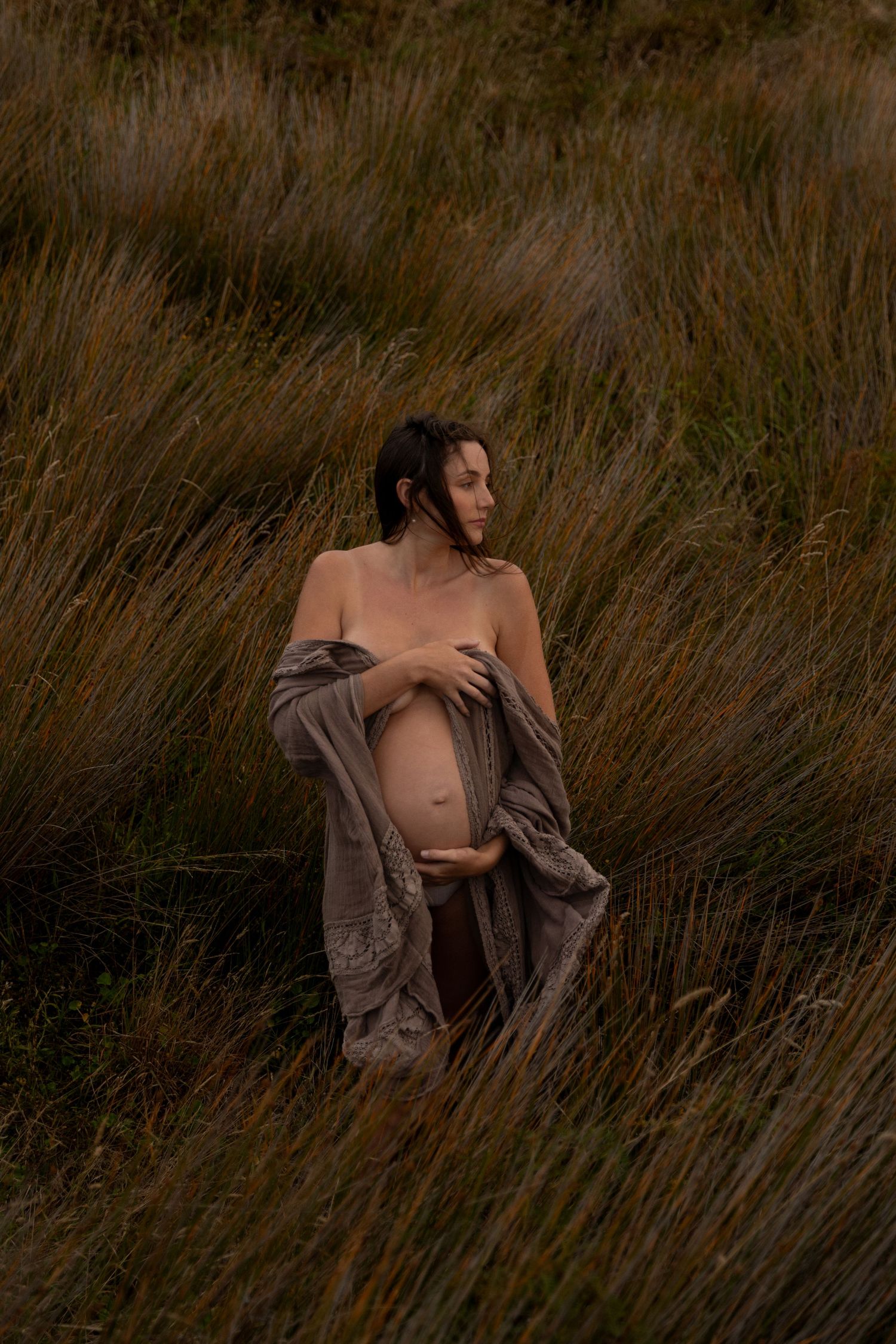 Artistic portrait in tall grass with muted earth tones and natural lighting.
