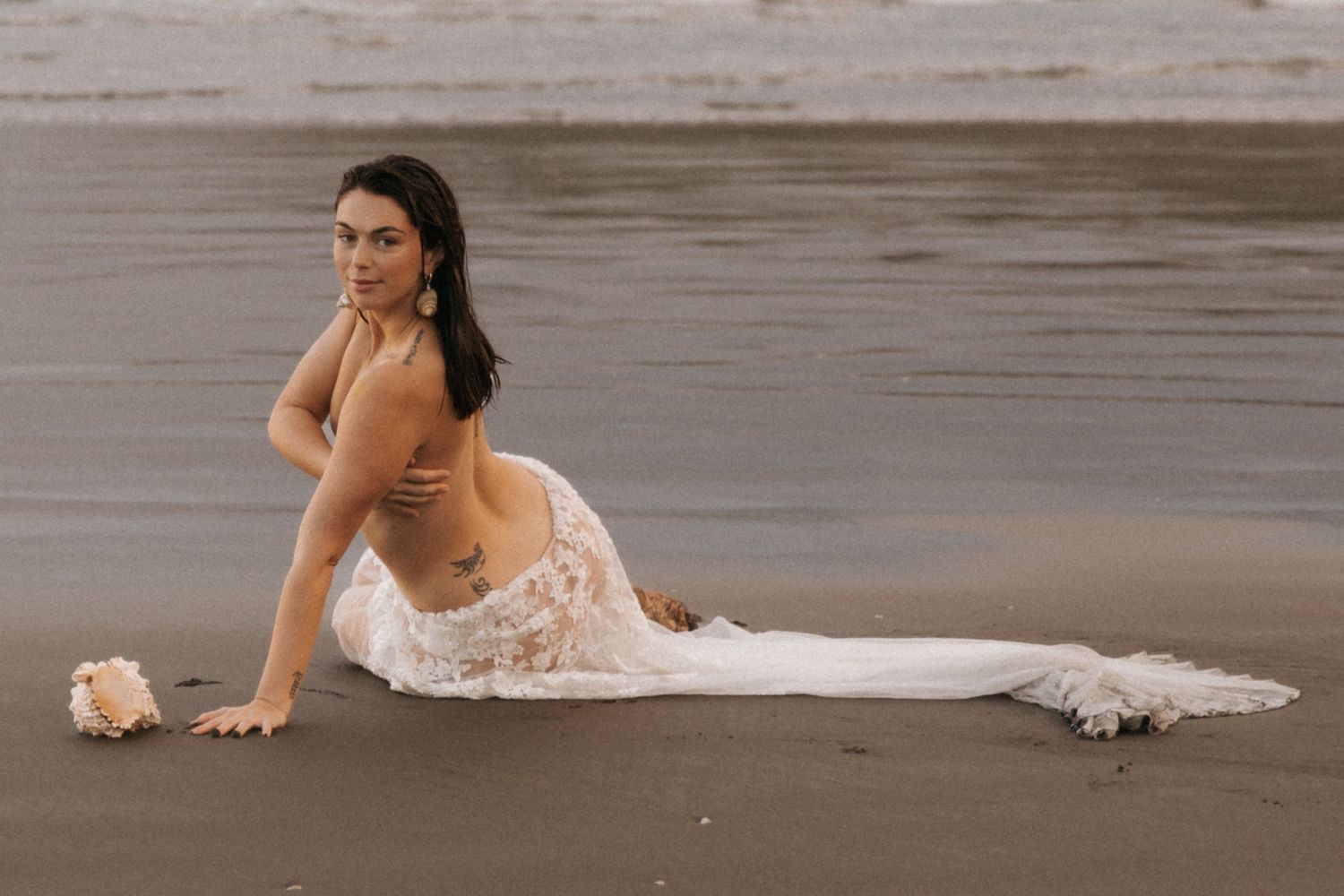 Elegant beach photography with white dress trailing in the sand at golden hour.
