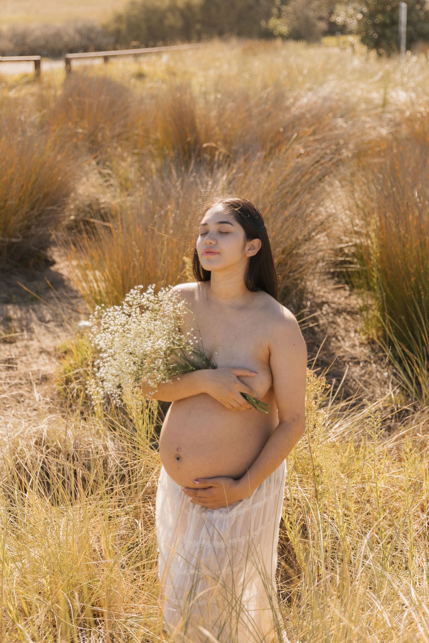 Delicate maternity photos with baby's breath flowers in a sun-kissed field.