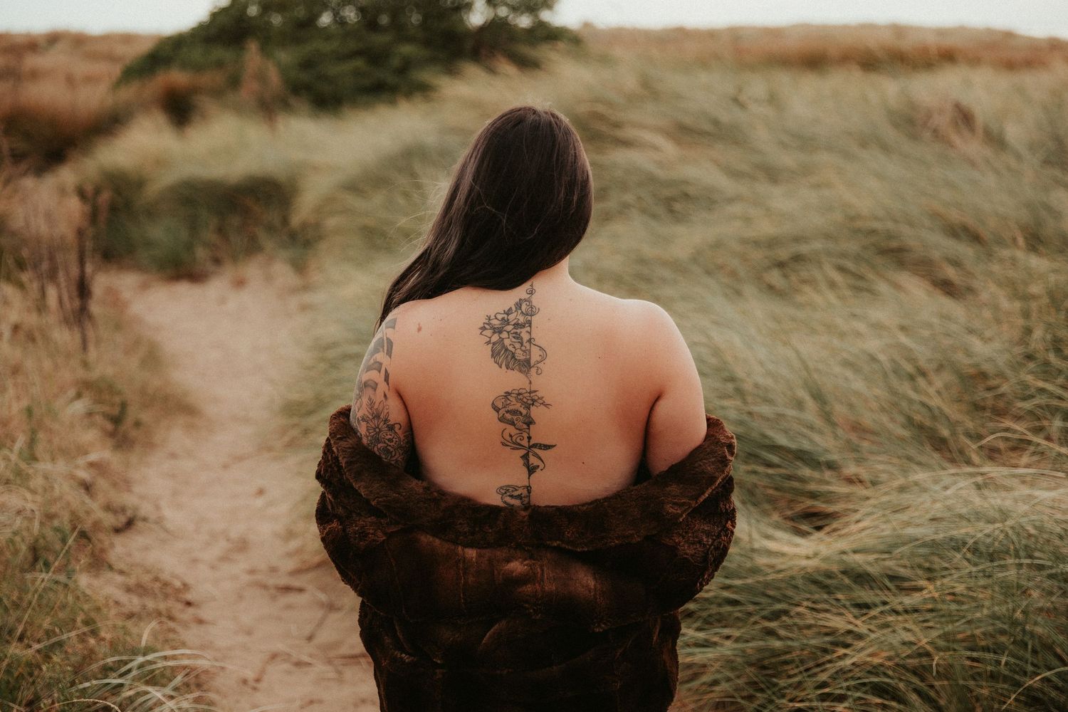 Artistic outdoor portraits showcasing tattoo details against natural grass backdrop.