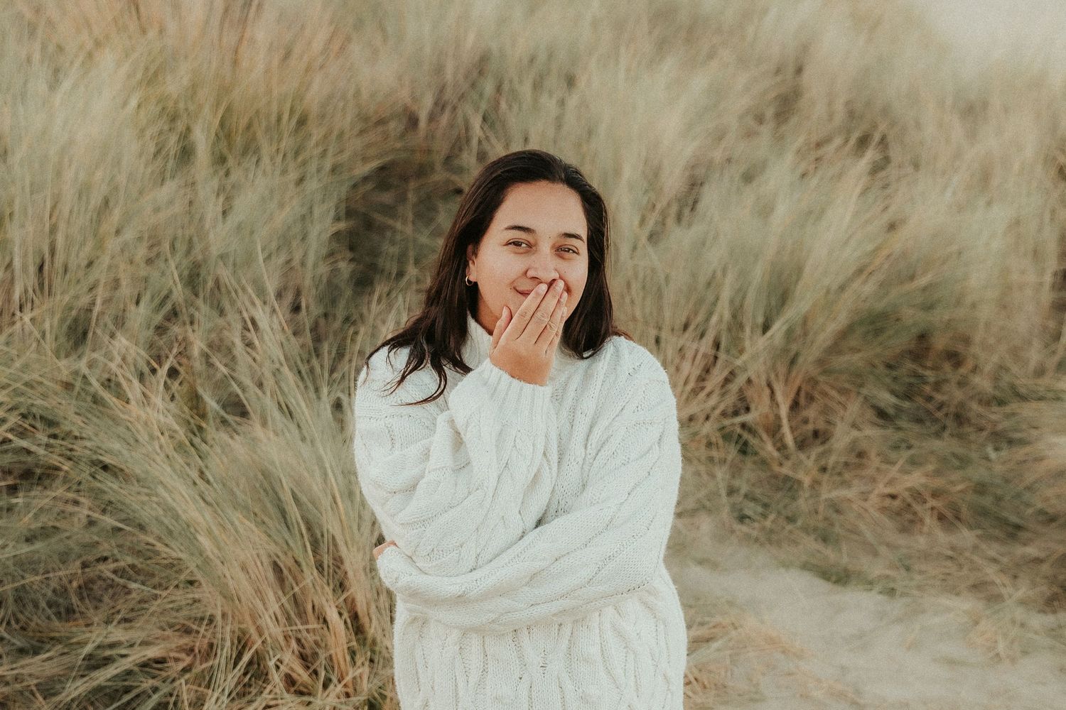 Person in white sweater poses against golden grass in natural outdoor setting.