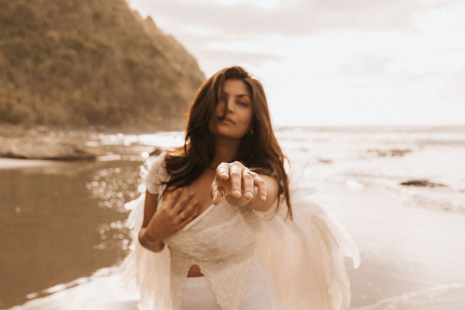 A woman in a flowing white dress dances gracefully on a sandy beach at sunset.
