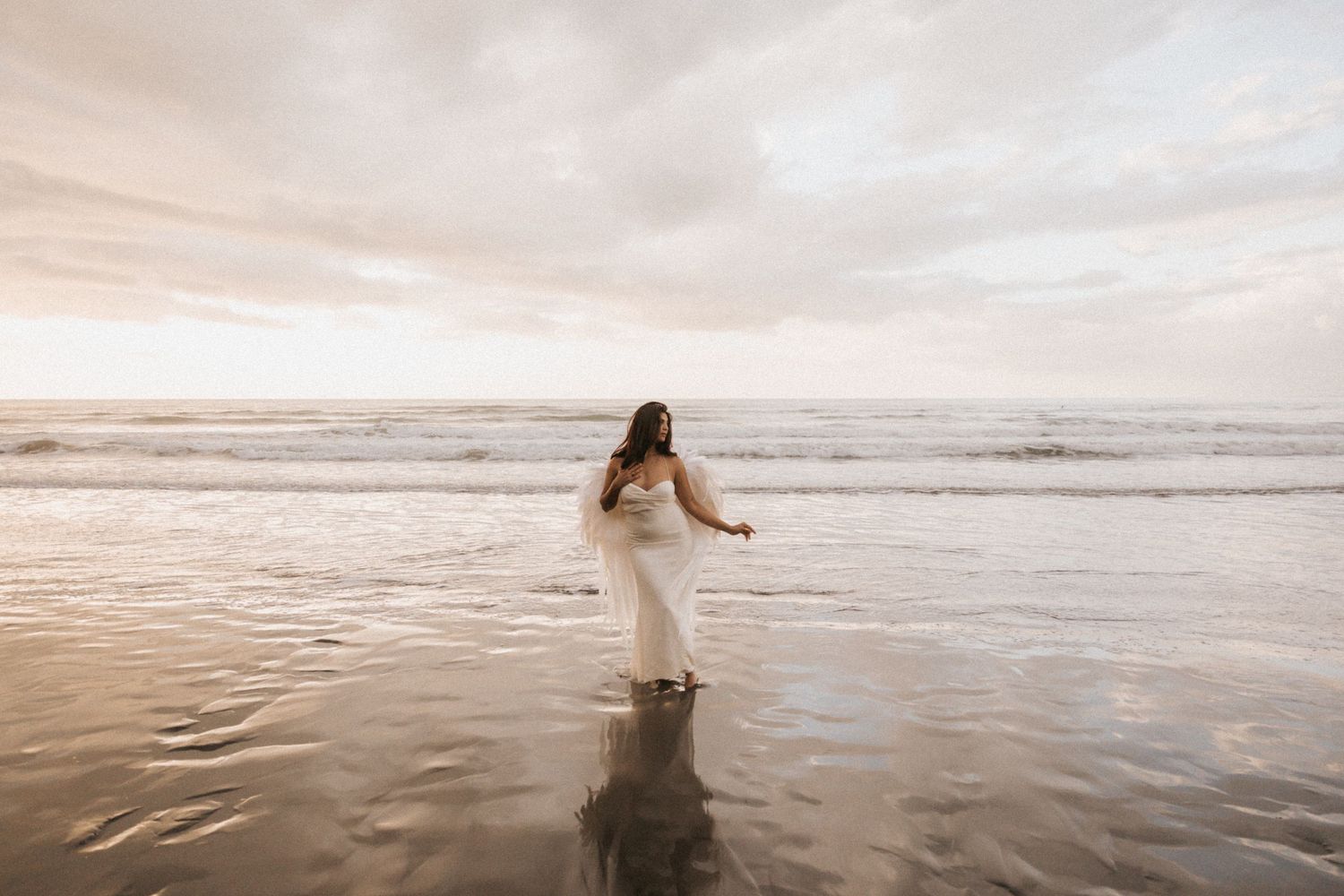 A person in a white dress walks along a misty beach shore during sunset creating a dreamy ethereal scene.